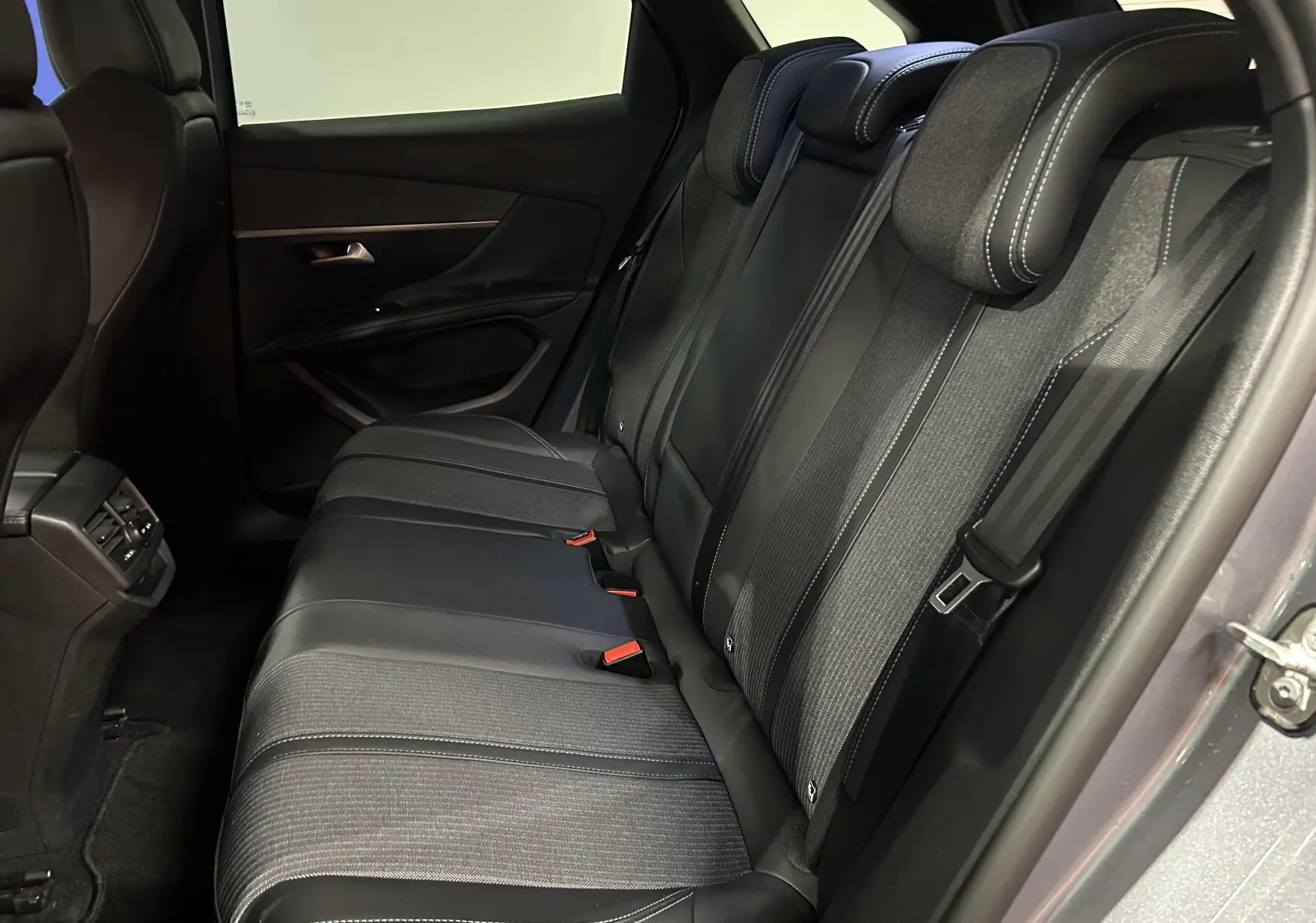 Vue latérale intérieure sur les sièges arrière en tissu et cuir noir du Peugeot 3008 gris Artense, porte arrière ouverte.