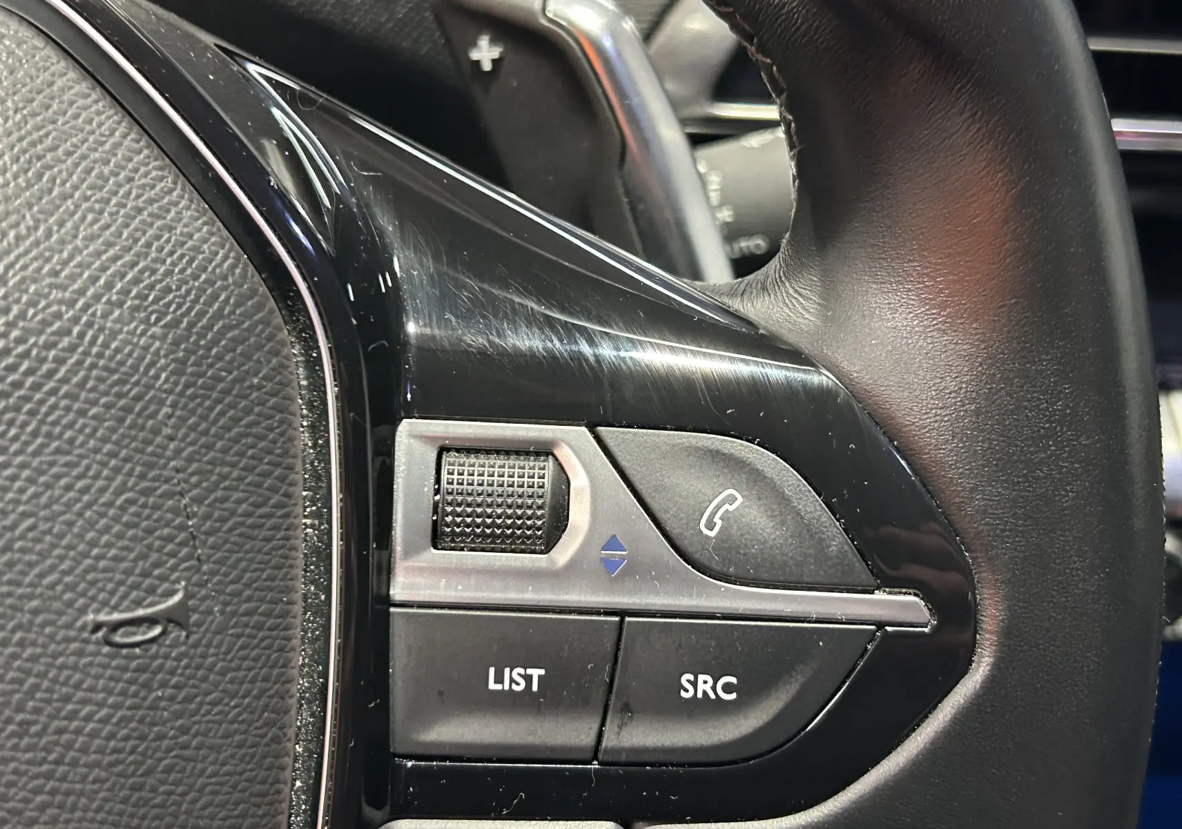 Gros plan sur les commandes gauche du volant en cuir noir du Peugeot 3008 gris Artense, avec molette et boutons fonction téléphone.