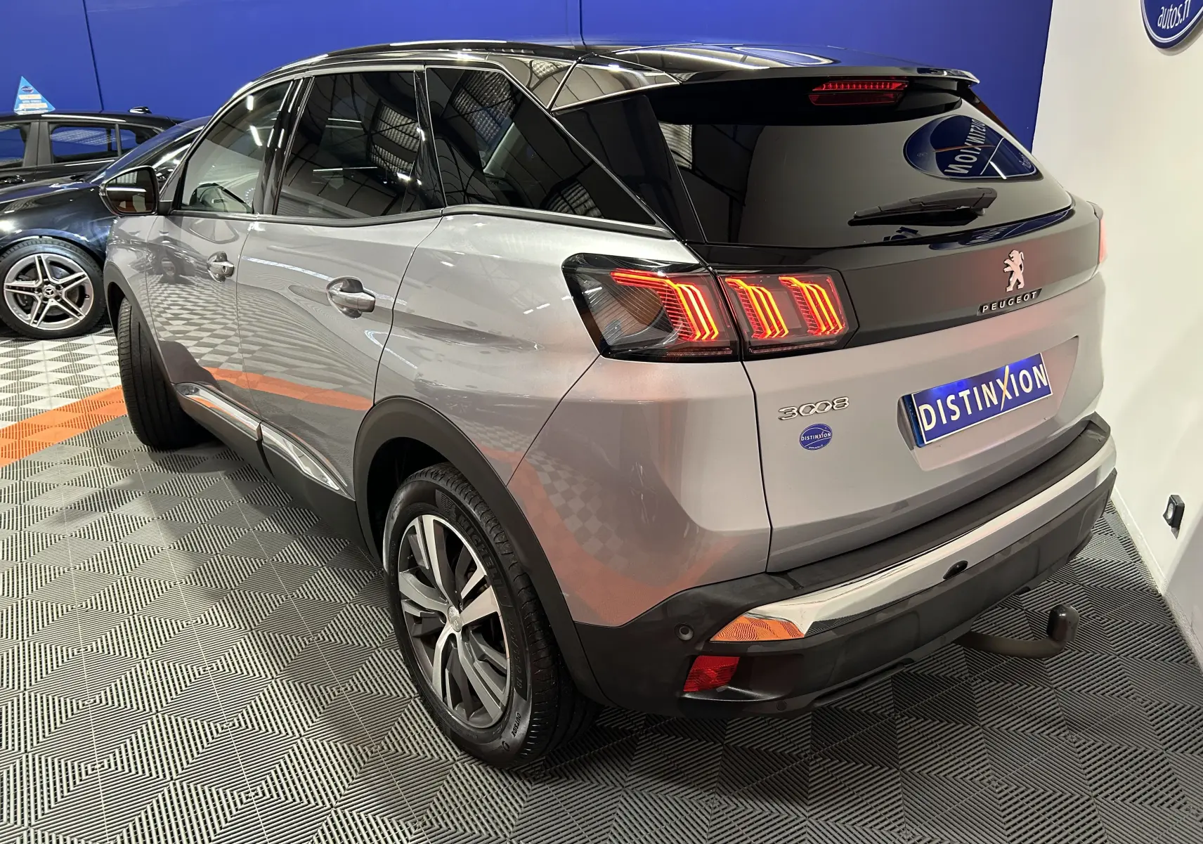 Vue 3/4 arrière droite d’un Peugeot 3008 gris Artense avec toit noir et attelage visible en intérieur showroom.