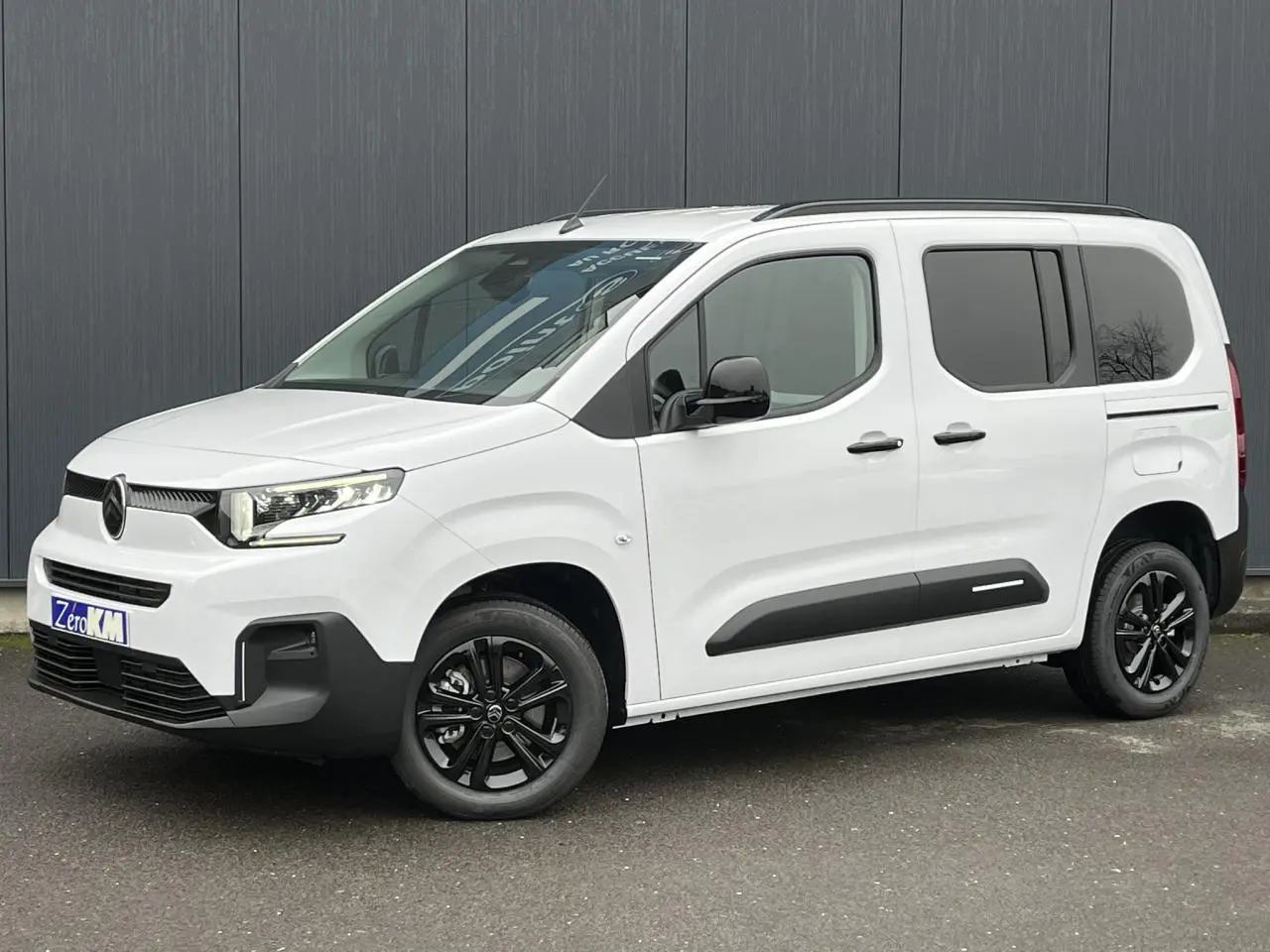 Vue 3/4 avant droite du Citroën Berlingo Multispace blanc glacier avec jantes noires et barres de toit noires.