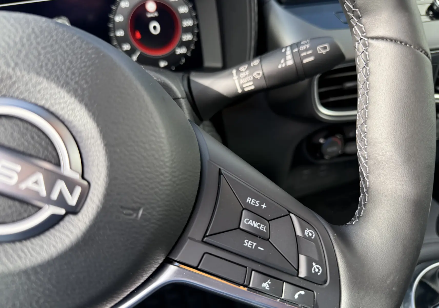 Gros plan sur le volant cuir noir du Nissan Juke 2025, avec commandes de régulateur de vitesse et téléphone intégrées.