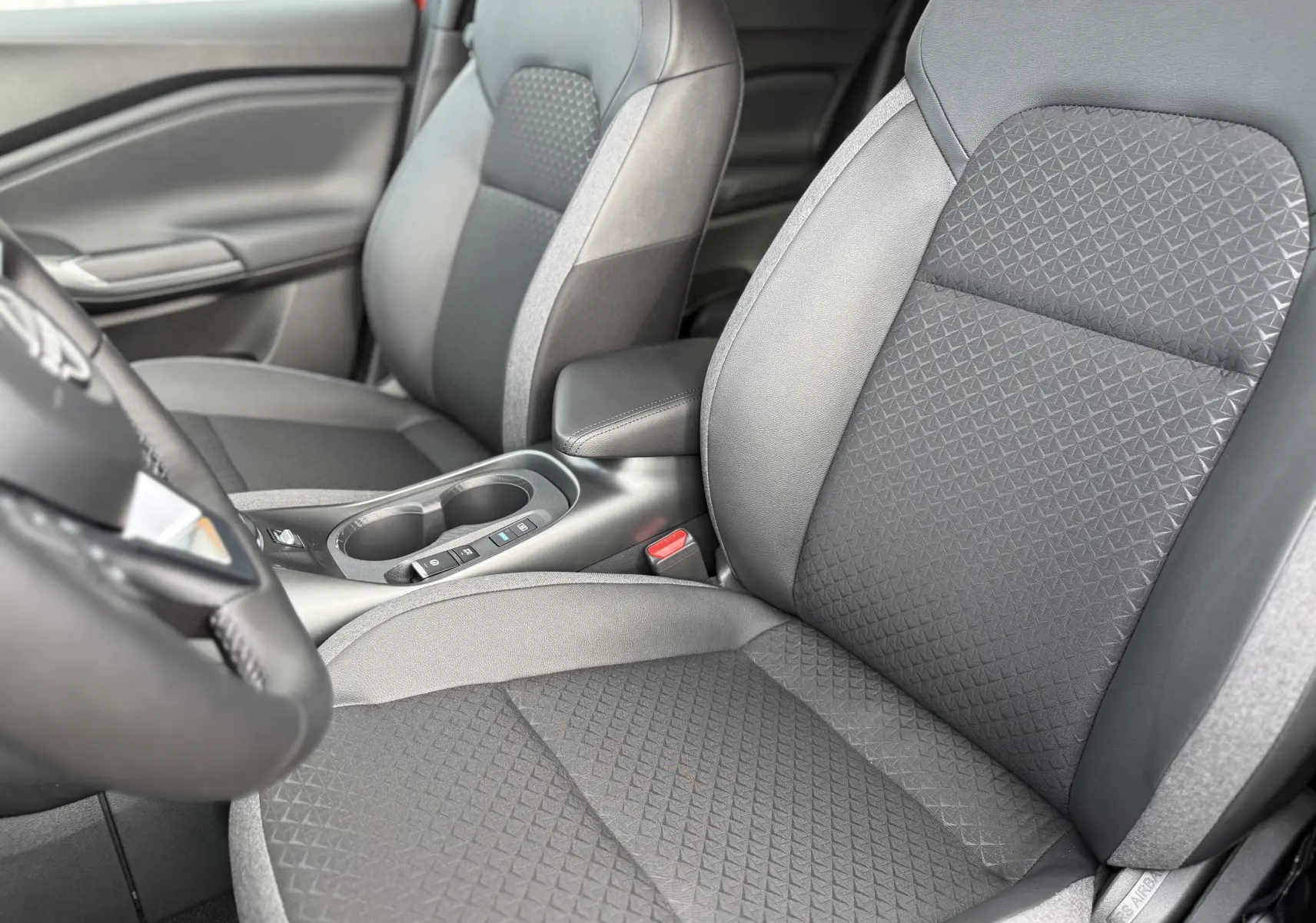 Vue rapprochée des sièges avant noirs et gris du Nissan Juke 2025, mettant en valeur la texture et l'accoudoir central.