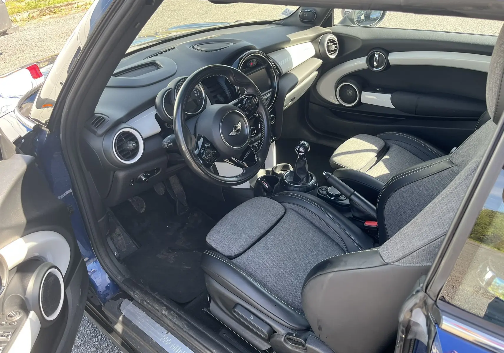 Intérieur côté conducteur d’une MINI Cabriolet bleu 2017, sellerie tissu/cuir gris noir avec tableau de bord moderne.