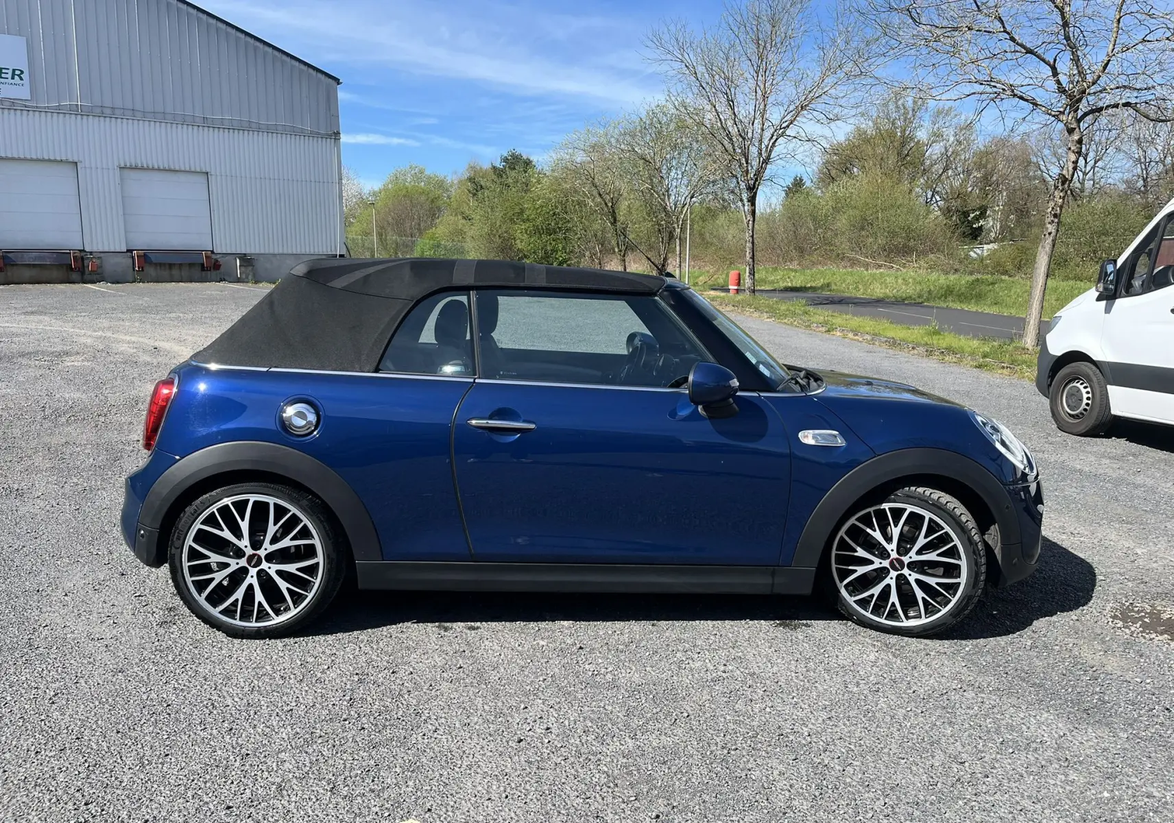 Vue de profil côté gauche d'une MINI Cabriolet F57 Cooper S bleu avec capote noire fermée et jantes alliage bicolores.