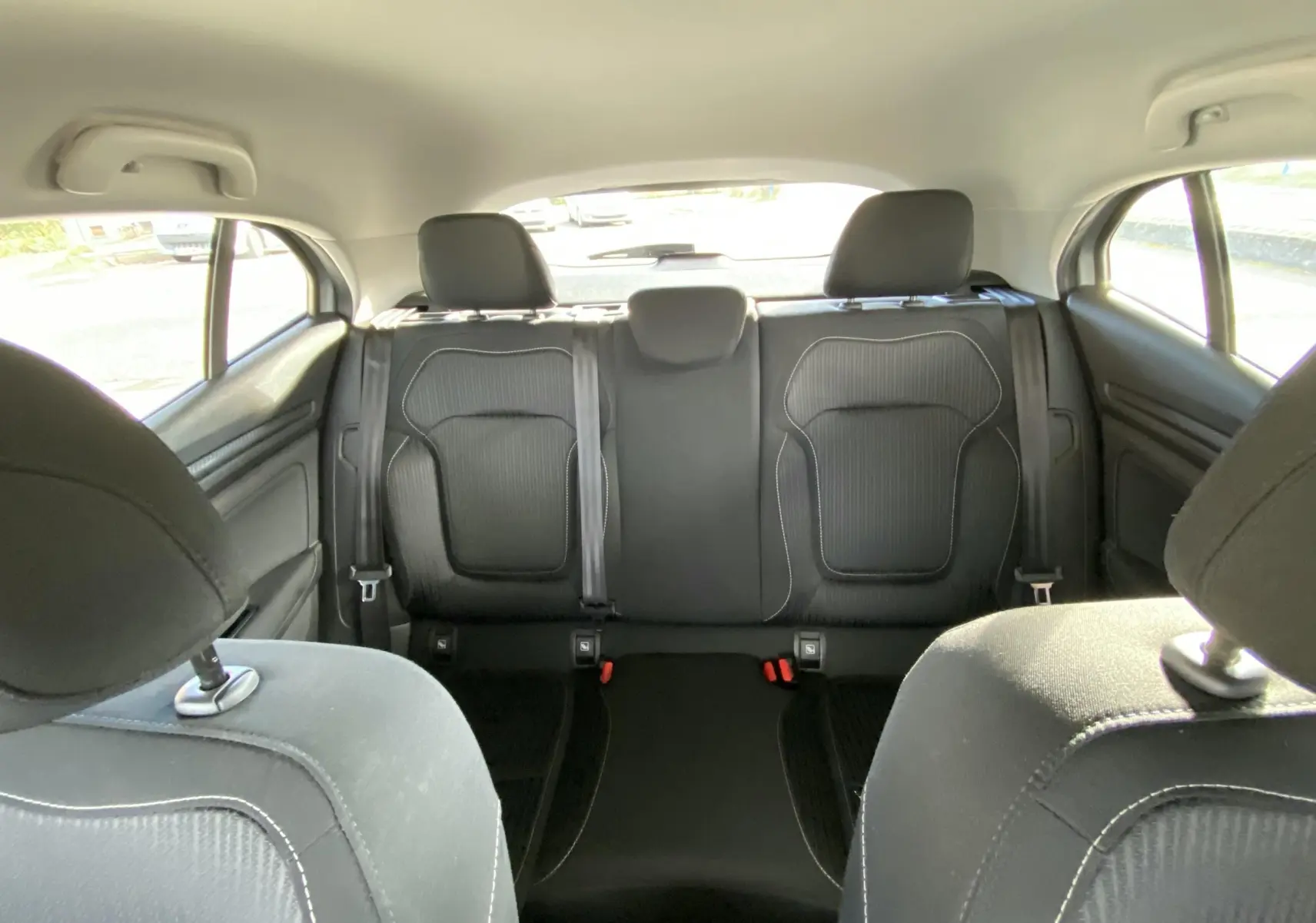 Vue intérieure arrière des sièges noirs en tissu de la Renault Mégane IV Berline gris, avec appuie-têtes et ceintures visibles.