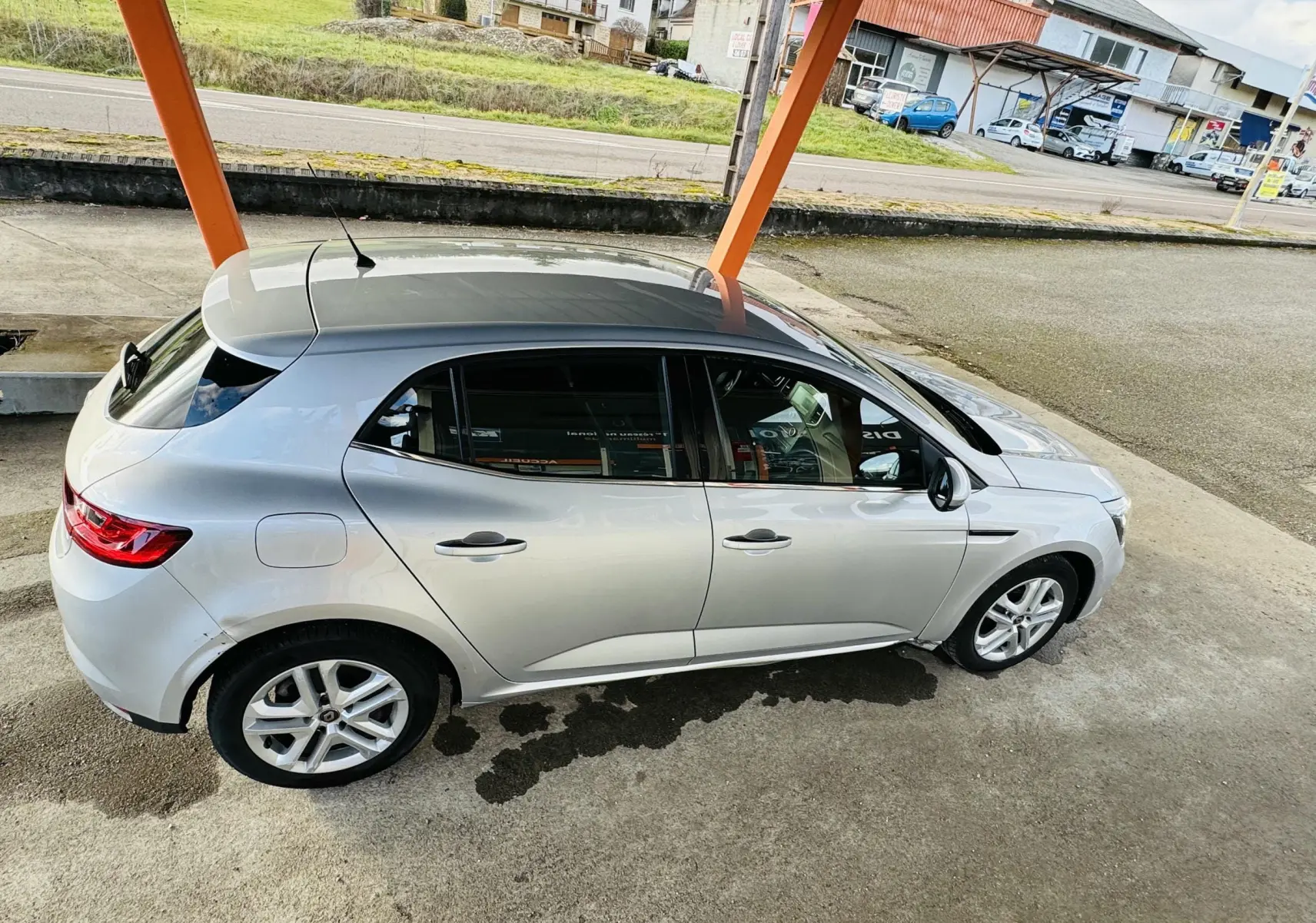 Vue de côté droit en léger plongé d'une Renault Mégane IV berline gris métallisé stationnée sous abri avec jantes alliage.