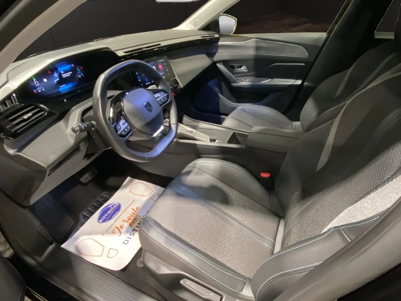 Intérieur noir de la Peugeot 308 2024, vue côté conducteur montrant le tableau de bord numérique et les sièges en tissu et cuir.