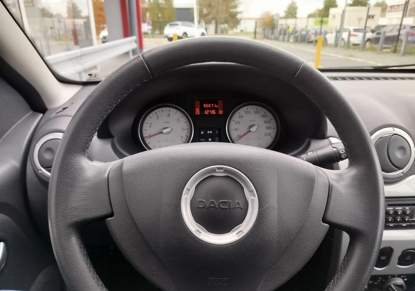 Vue centrée sur le volant noir en cuir de la Dacia Sandero 2011, avec tableau de bord et compteurs blancs visibles.