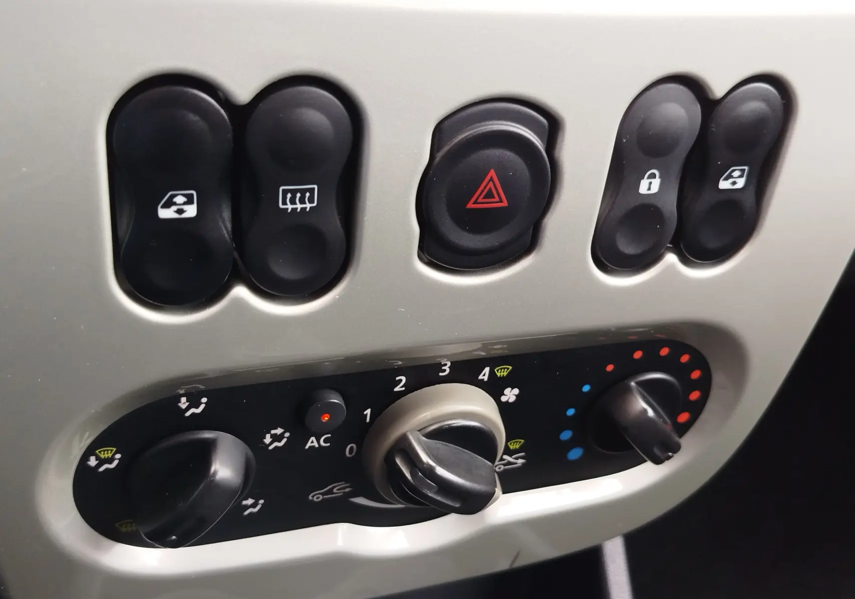 Gros plan sur la console centrale de la Dacia Sandero noire, montrant les commandes de climatisation et les boutons de verrouillage et dégivrage.