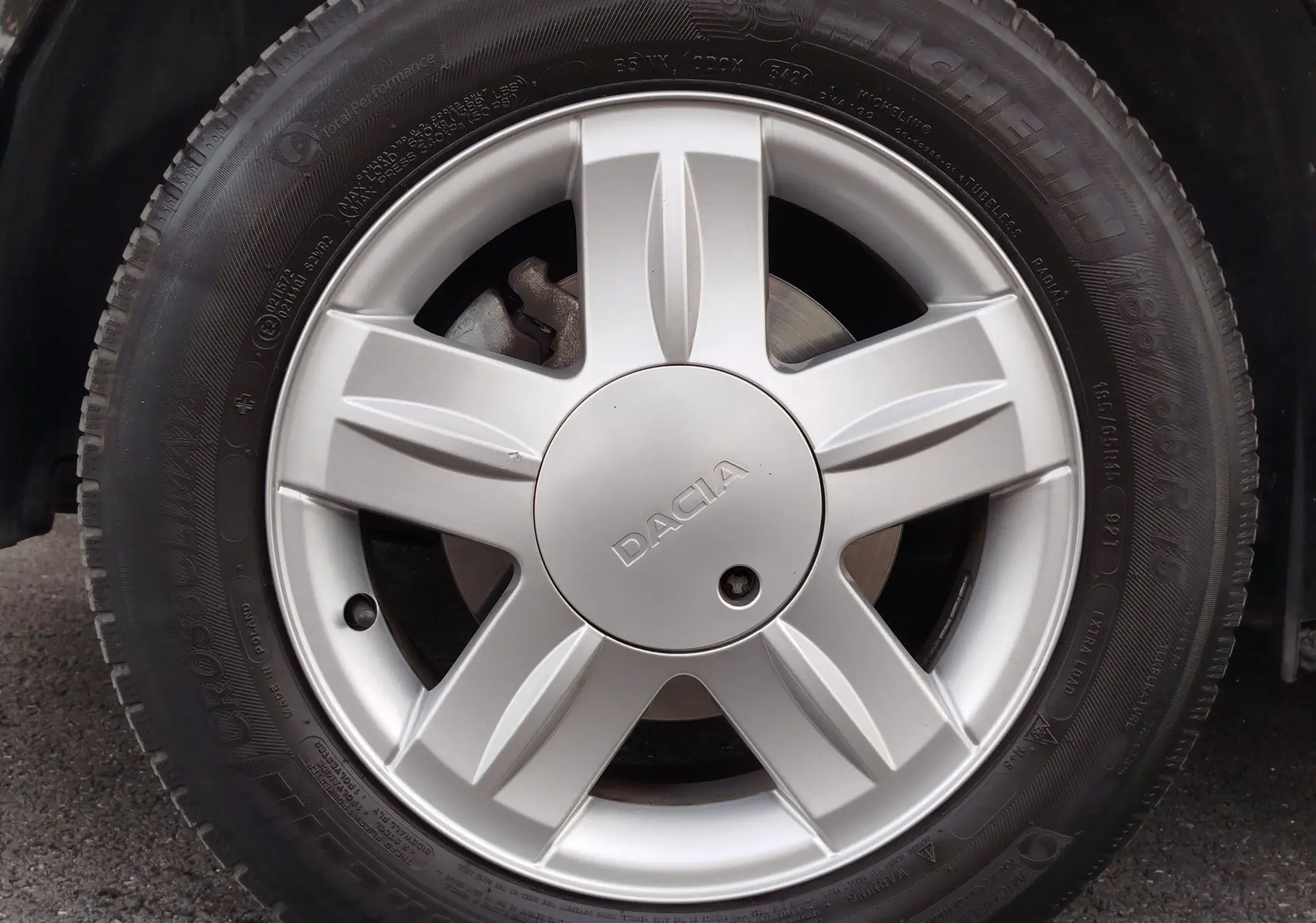 Gros plan sur la roue avant gauche de la Dacia Sandero noire, avec jante argentée et logo central DACIA visible.