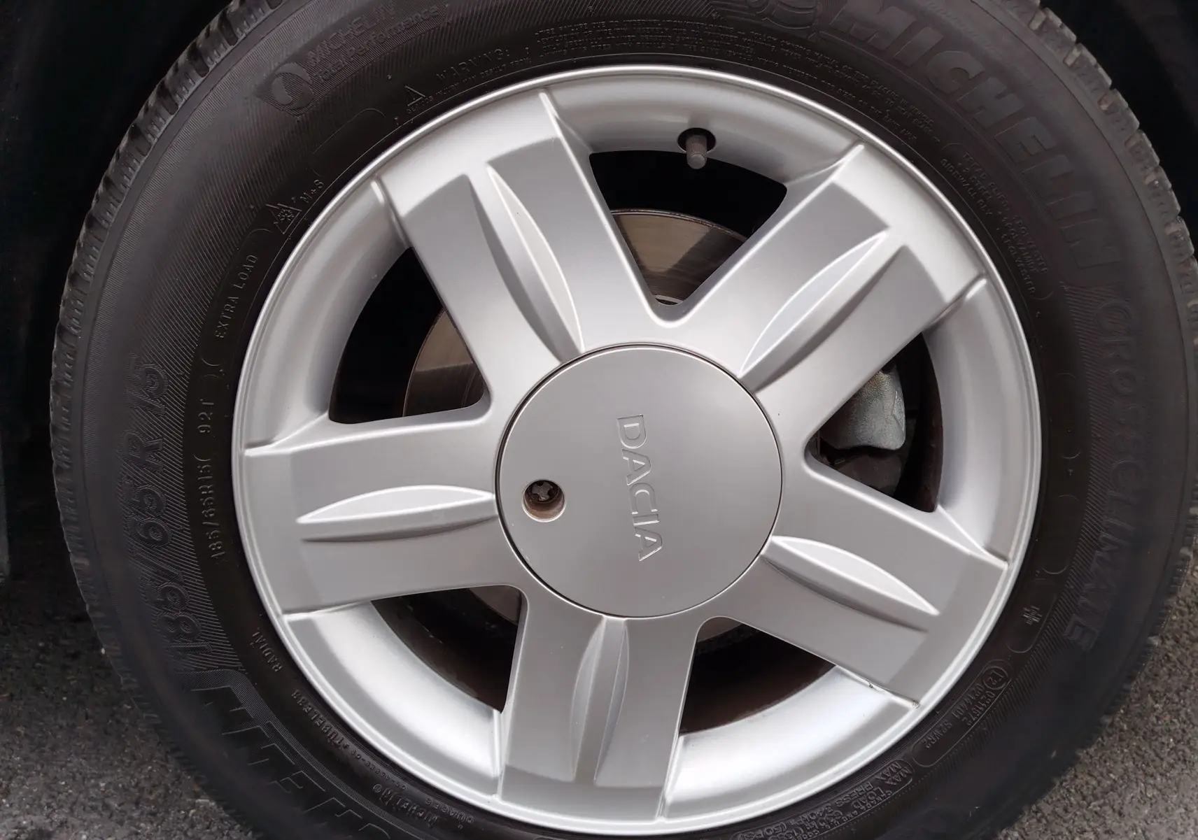 Gros plan sur la jante argentée de la DACIA Sandero noire, mettant en valeur le logo central et le pneu Michelin.