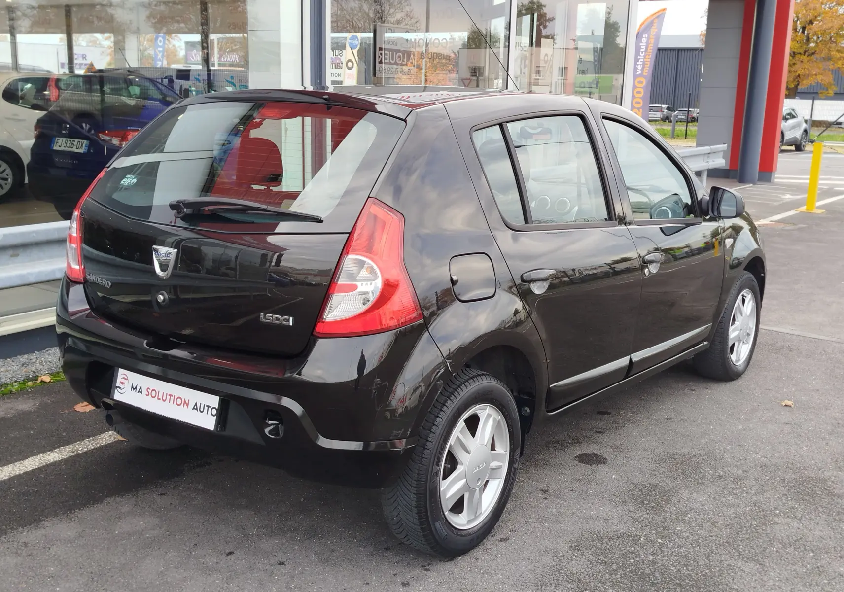 Vue 3/4 arrière droite d'une Dacia Sandero noire de 2011, cinq portes, avec jantes alliage et feux arrière distinctifs.