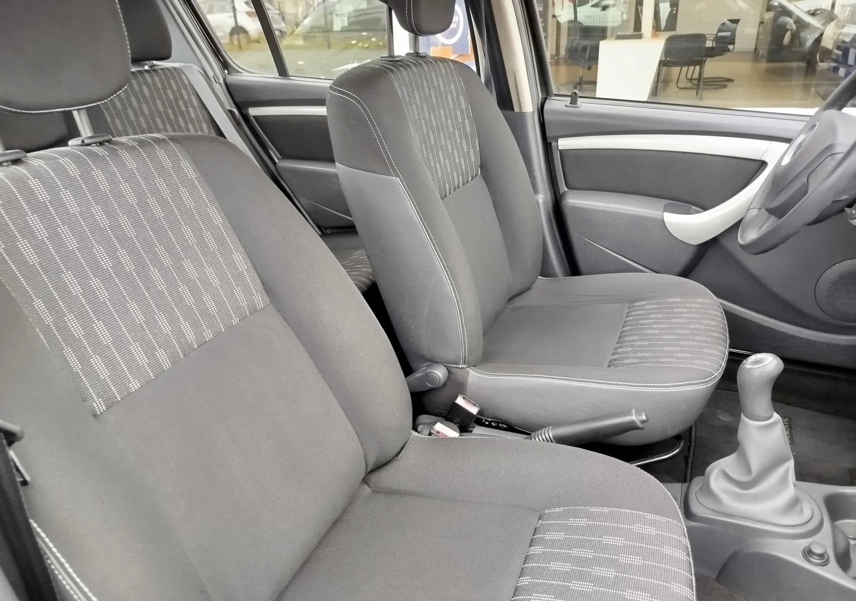 Intérieur de la Dacia Sandero noire 2011, vue côté droit sur les sièges avant en tissu gris avec volant cuir et levier de vitesse manuel.