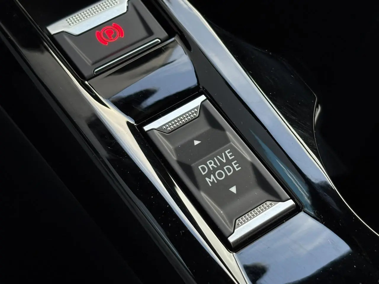 Gros plan sur la console centrale noire brillante du Peugeot 2008 Hybrid 145 avec bouton Drive Mode et frein de stationnement électrique.