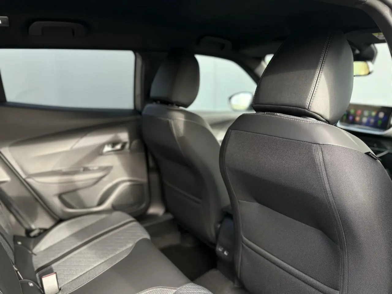 Vue intérieure arrière côté gauche du Peugeot 2008 Hybrid 145 e-DSC6 Allure avec sièges noirs et ciel de pavillon sombre.