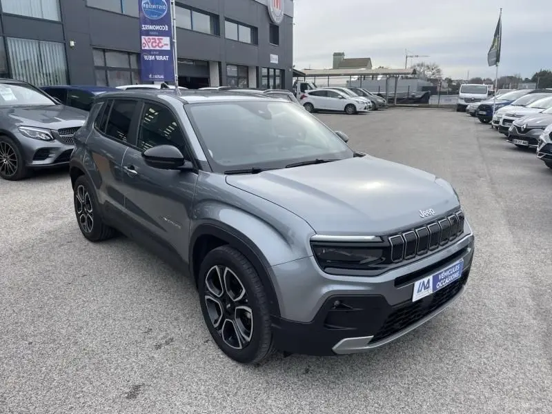 Jeep Avenger gris métal en vue 3/4 avant droit, avec calandre distinctive et jantes noires à motifs argentés.