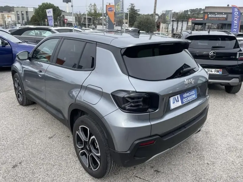 Jeep Avenger gris métal vu en 3/4 arrière droit, avec feux arrière noirs et vitres teintées, stationné en extérieur.