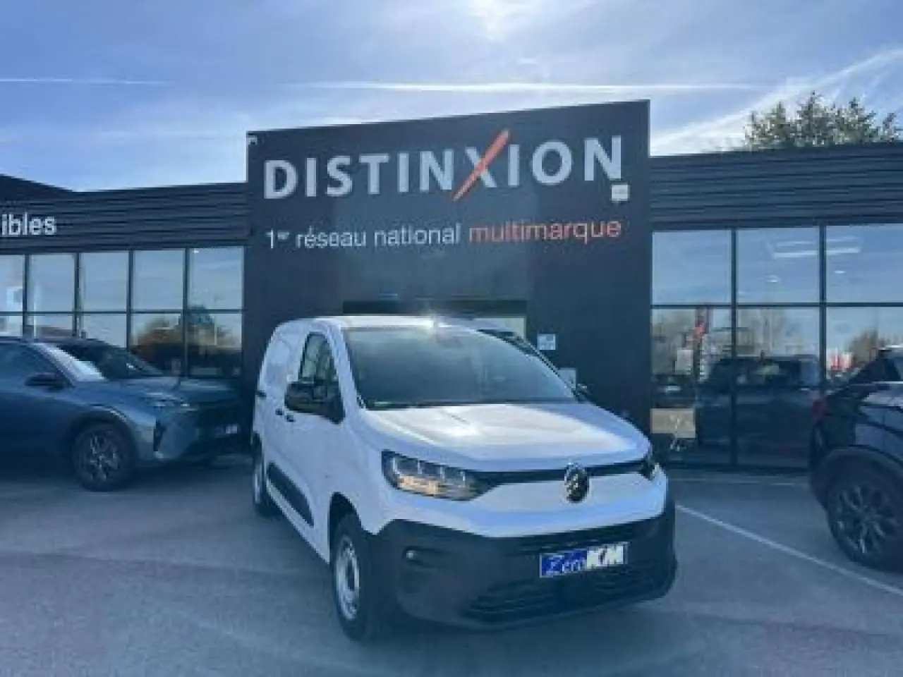 Vue 3/4 avant d'un utilitaire Citroën Berlingo blanc Icy avec pare-chocs noir devant un bâtiment Distinxion.