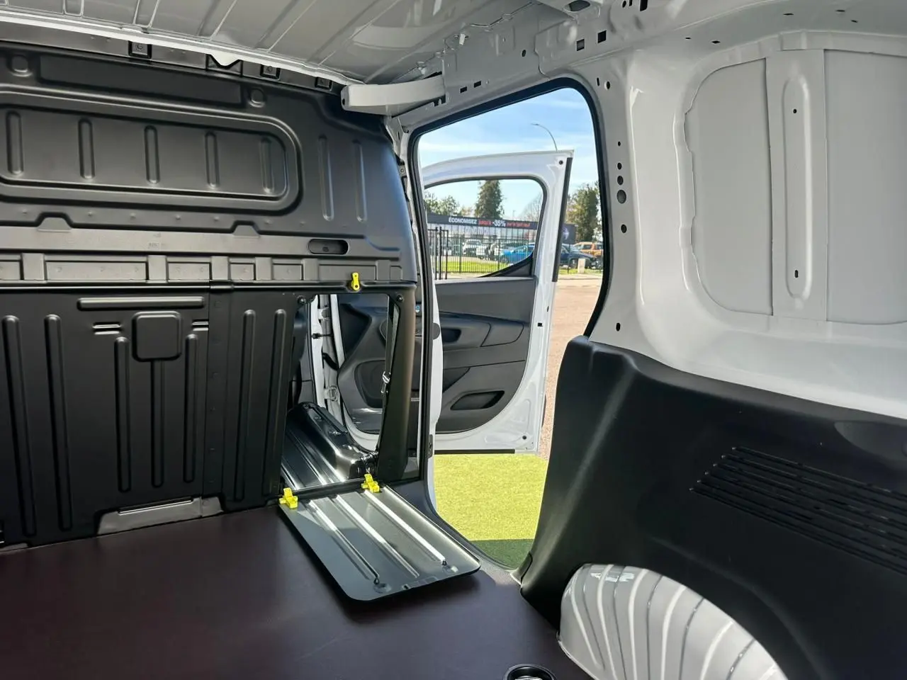 Vue intérieure arrière du Citroën Berlingo blanc Icy, porte latérale droite ouverte et cloison cabine partiellement rabattue.