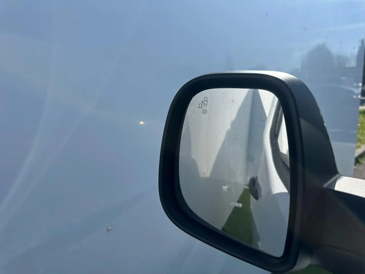 Rétroviseur droit noir brillant du Citroën Berlingo blanc Icy, vue rapprochée sur fond de carrosserie blanche.