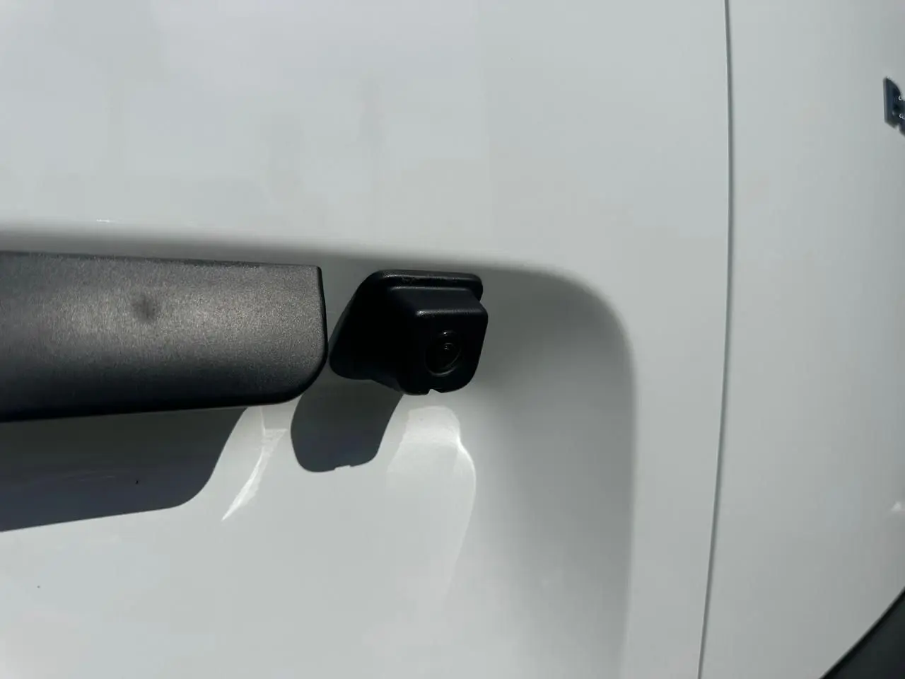 Gros plan sur la caméra de recul noire intégrée à la porte latérale blanche du Citroën Berlingo III Van.