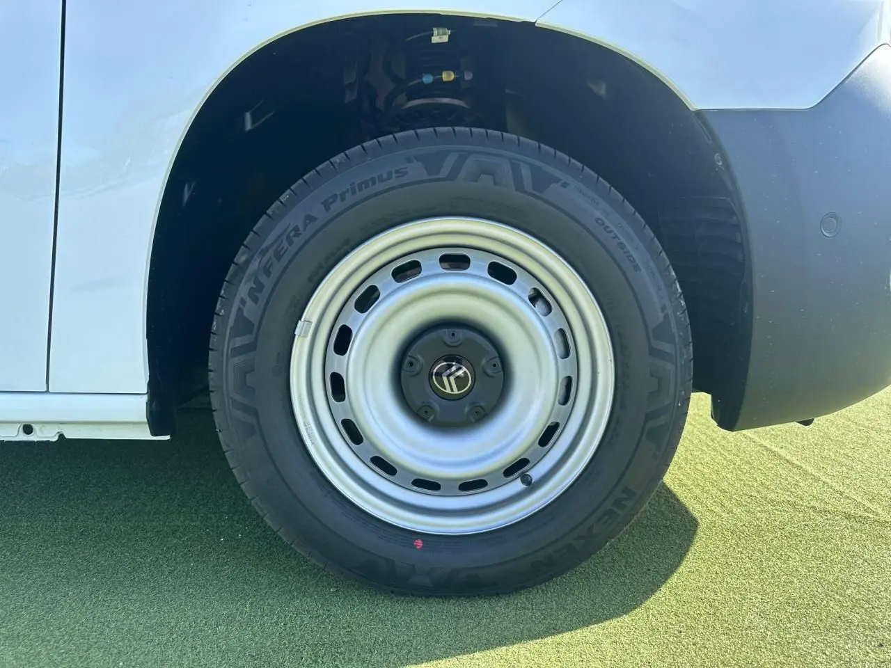 Gros plan sur la roue avant droite acier grise du Citroën Berlingo blanc Icy, avec pneu Nexen sur sol vert.