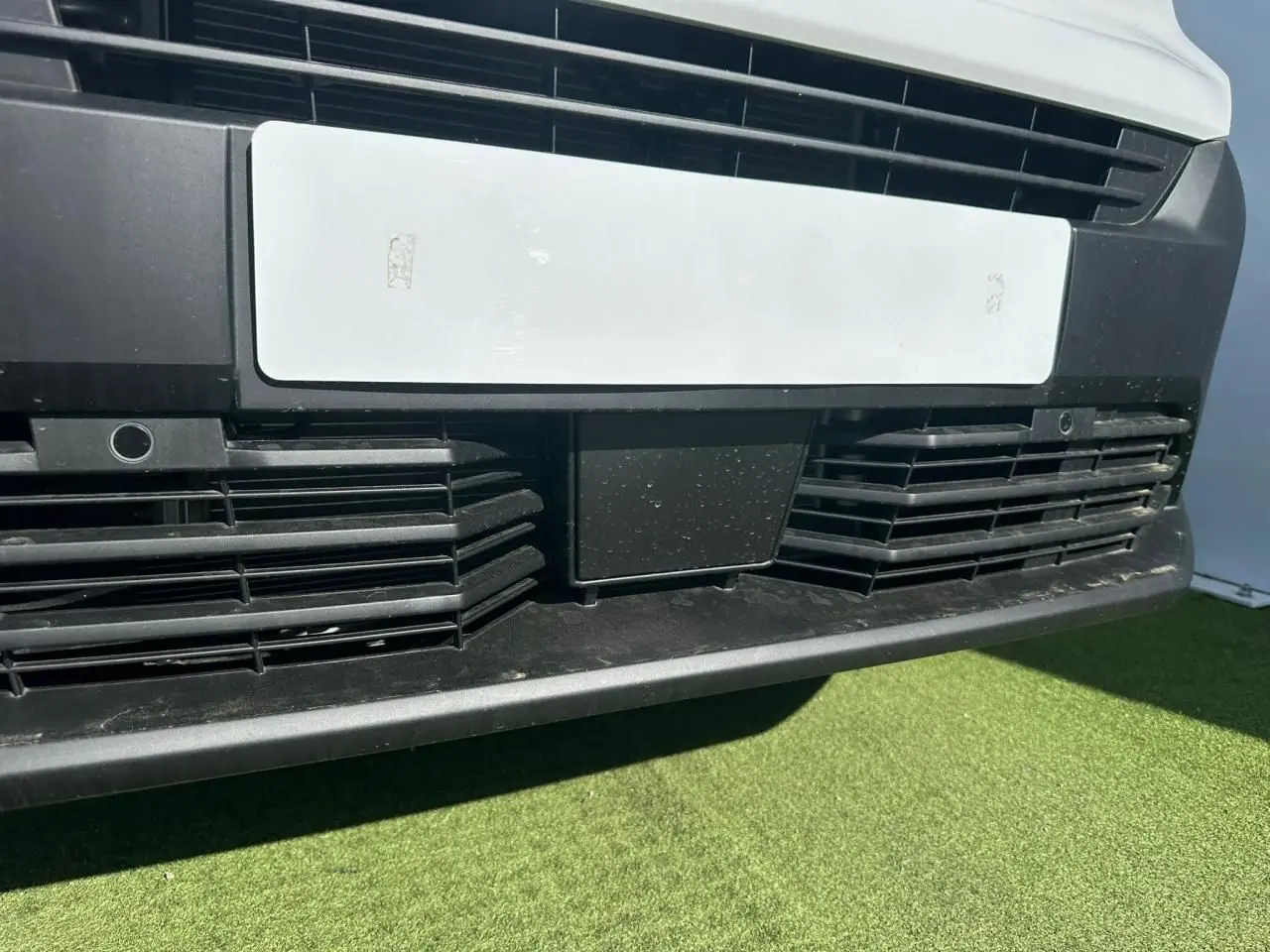 Gros plan sur la calandre avant noire et la plaque blanche du Citroën Berlingo III blanc Icy, vue de face basse.