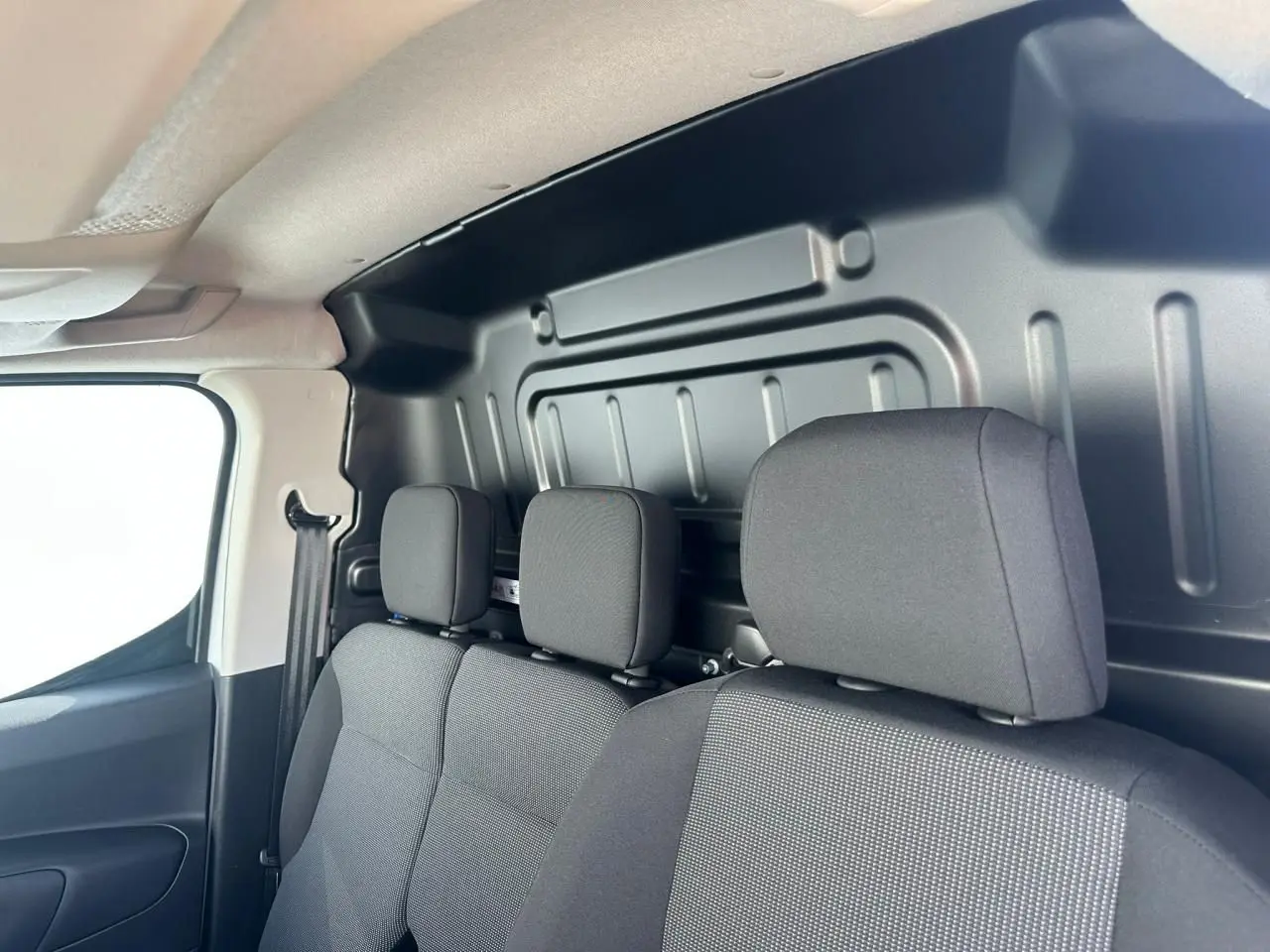 Vue intérieure côté droit du Citroën Berlingo blanc, montrant les sièges avant en tissu gris et cloison métallique arrière.