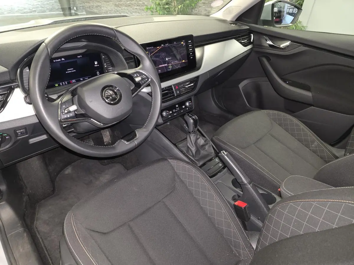 Vue intérieure côté conducteur du Skoda Kamiq 2023, montrant le volant cuir, tableau de bord digital et sièges tissu noirs.