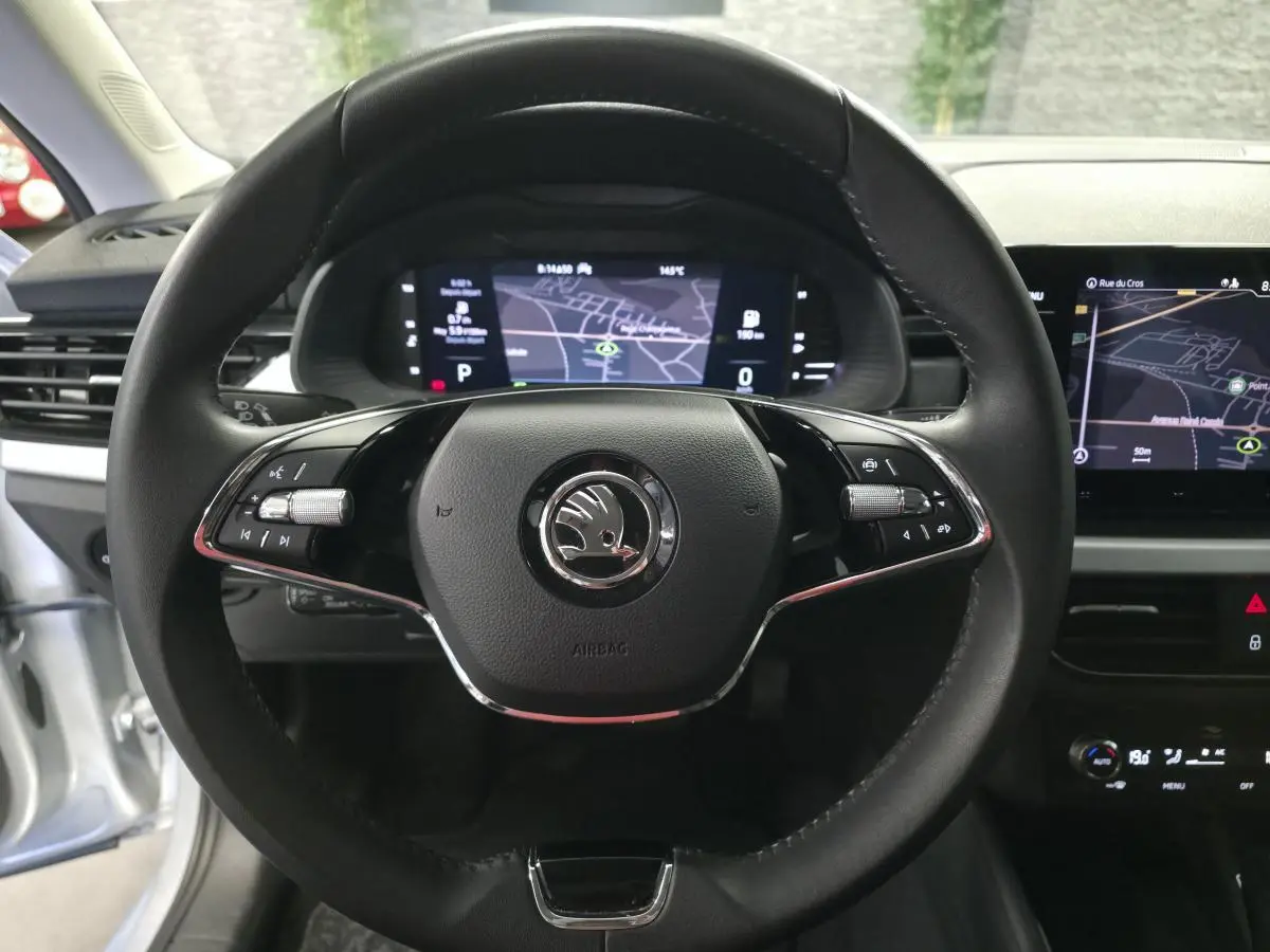 Vue intérieure centrée sur le volant cuir noir du Skoda Kamiq 2023 avec tableau de bord digital et écran de navigation.