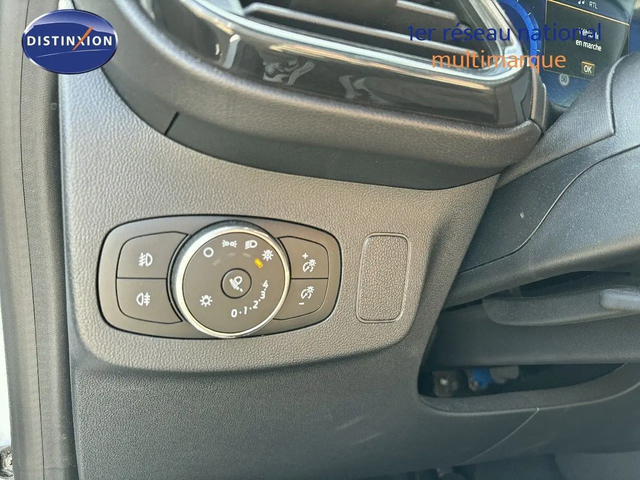 Gros plan sur le bouton de réglage des phares à gauche du volant dans l'habitacle du Ford Puma blanc 2022.