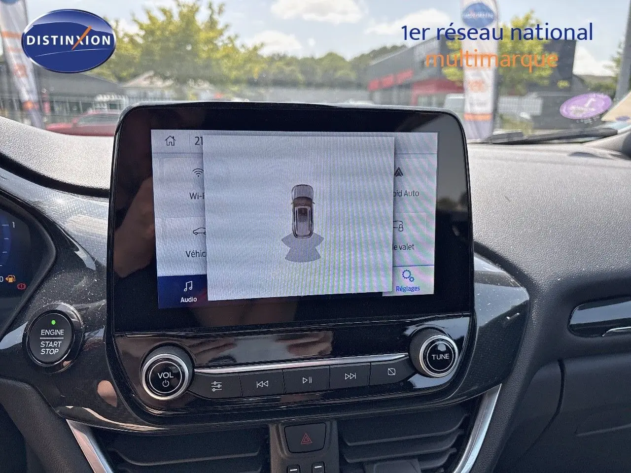 Vue intérieure centrée sur l'écran tactile du tableau de bord d'une Ford Puma blanche, affichant l'aide au stationnement.