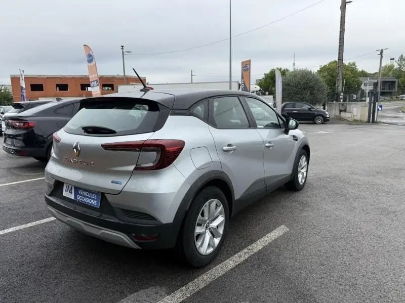 Vue 3/4 arrière droite d'un Renault Captur E-Tech 145 Zen gris métal 2022 avec toit noir sur parking humide.