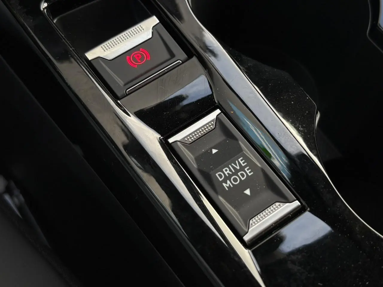Gros plan sur la console centrale noire brillante du Peugeot 2008 Hybrid avec bouton Drive Mode et frein de stationnement électrique.