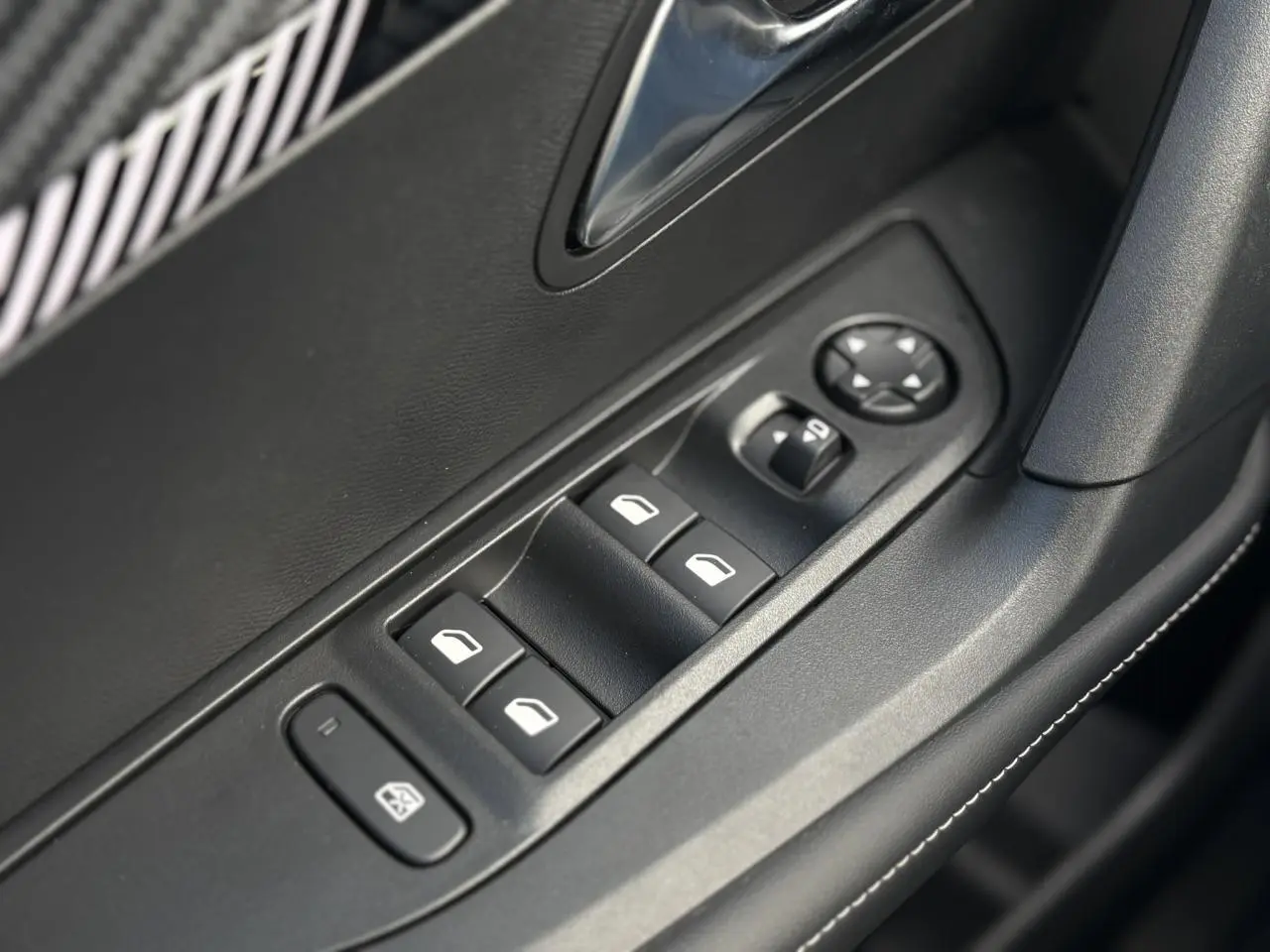 Gros plan sur les commandes de lève-vitres électriques côté conducteur, finition noire avec surpiqûres blanches.