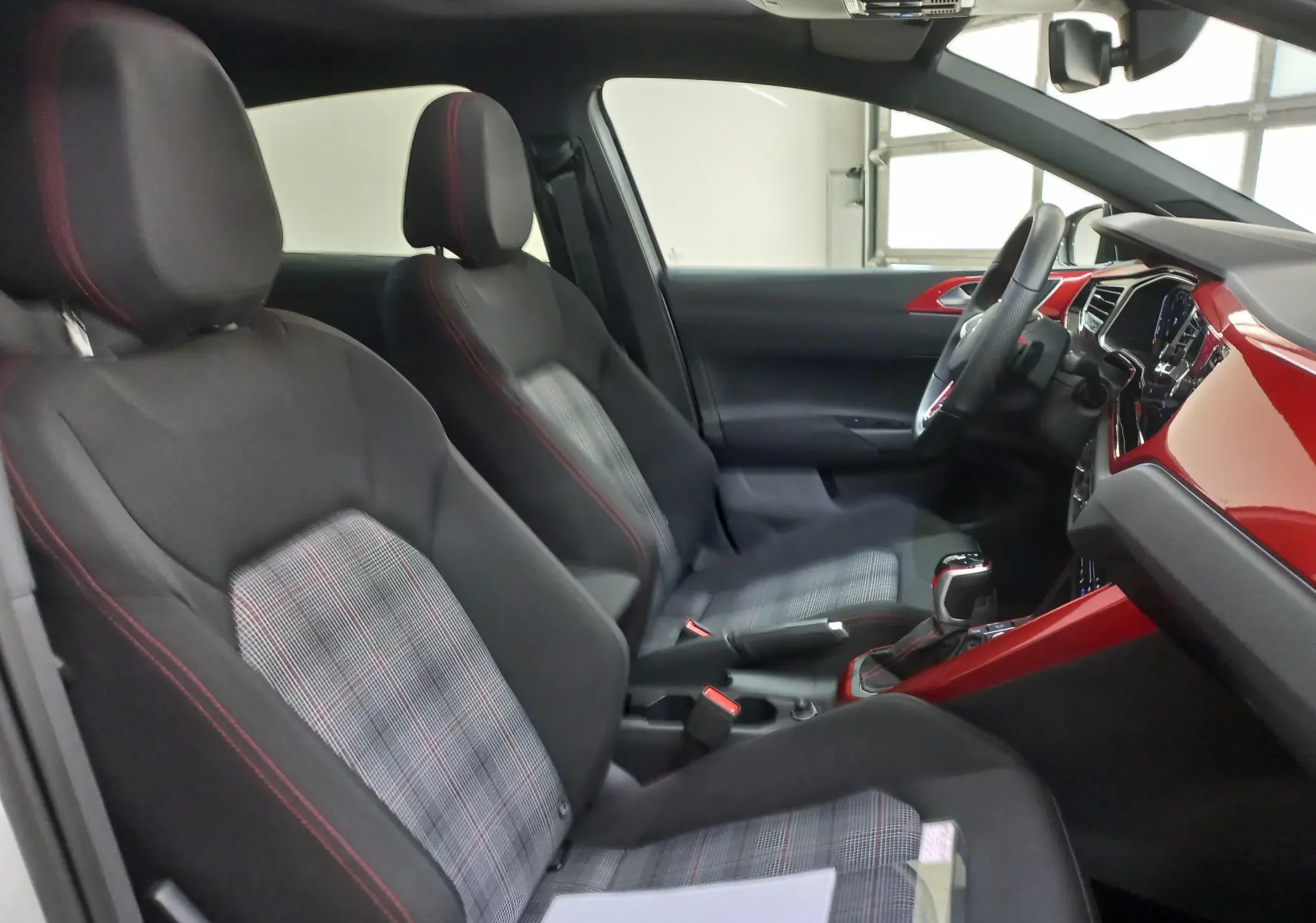 Vue intérieure côté gauche de la Volkswagen Polo GTI 2024, sièges noirs à motif écossais et tableau de bord rouge brillant.