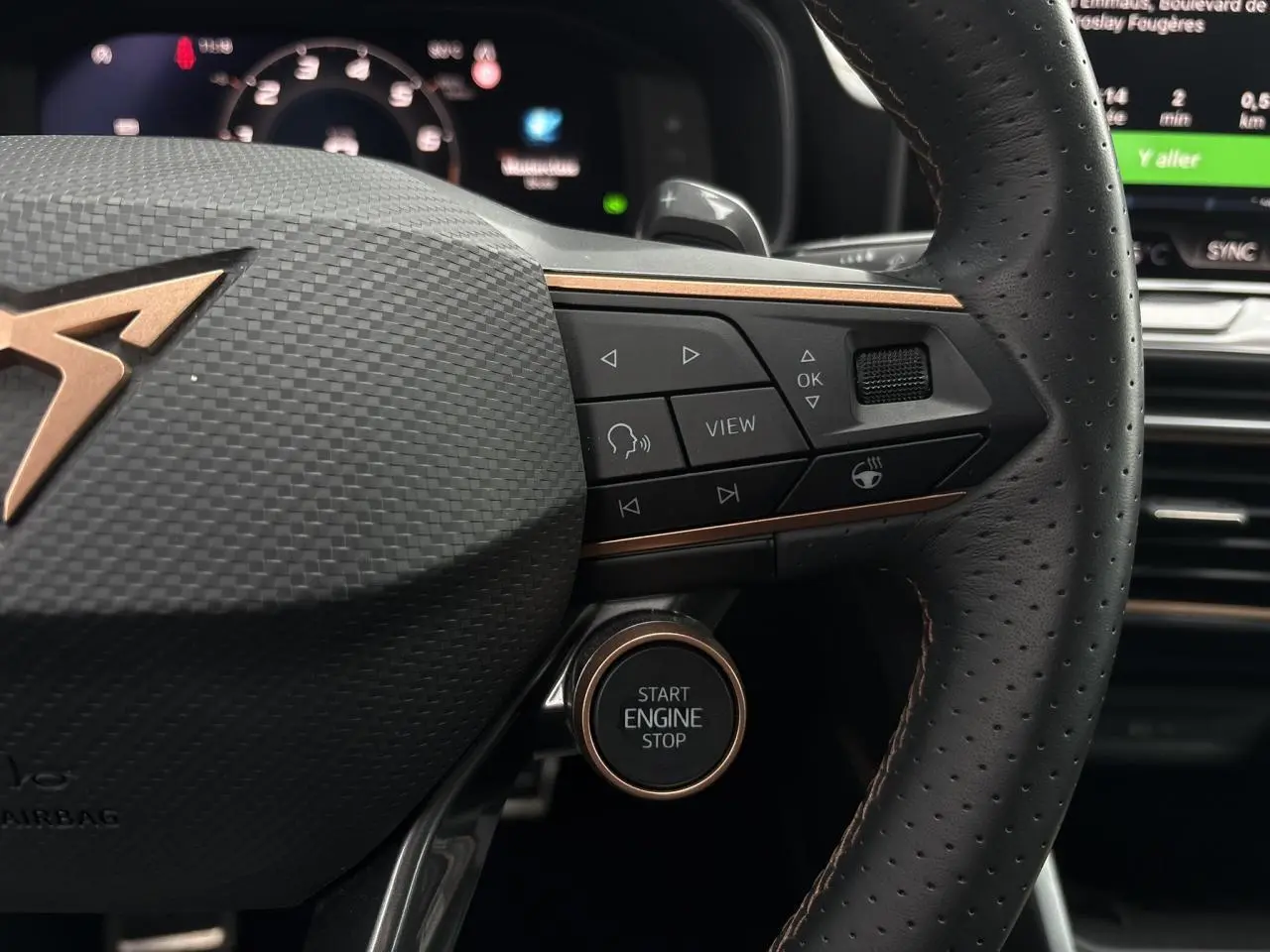 Gros plan sur le volant cuir perforé et le bouton Start Engine Stop du CUPRA LEON ST 2025, détails en cuivre et commandes intégrées.