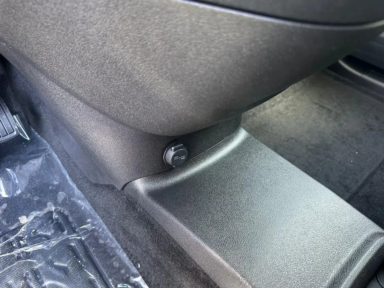 Prise 12V noire sur console centrale côté passager du Citroën Berlingo III blanc, plancher moquette visible.