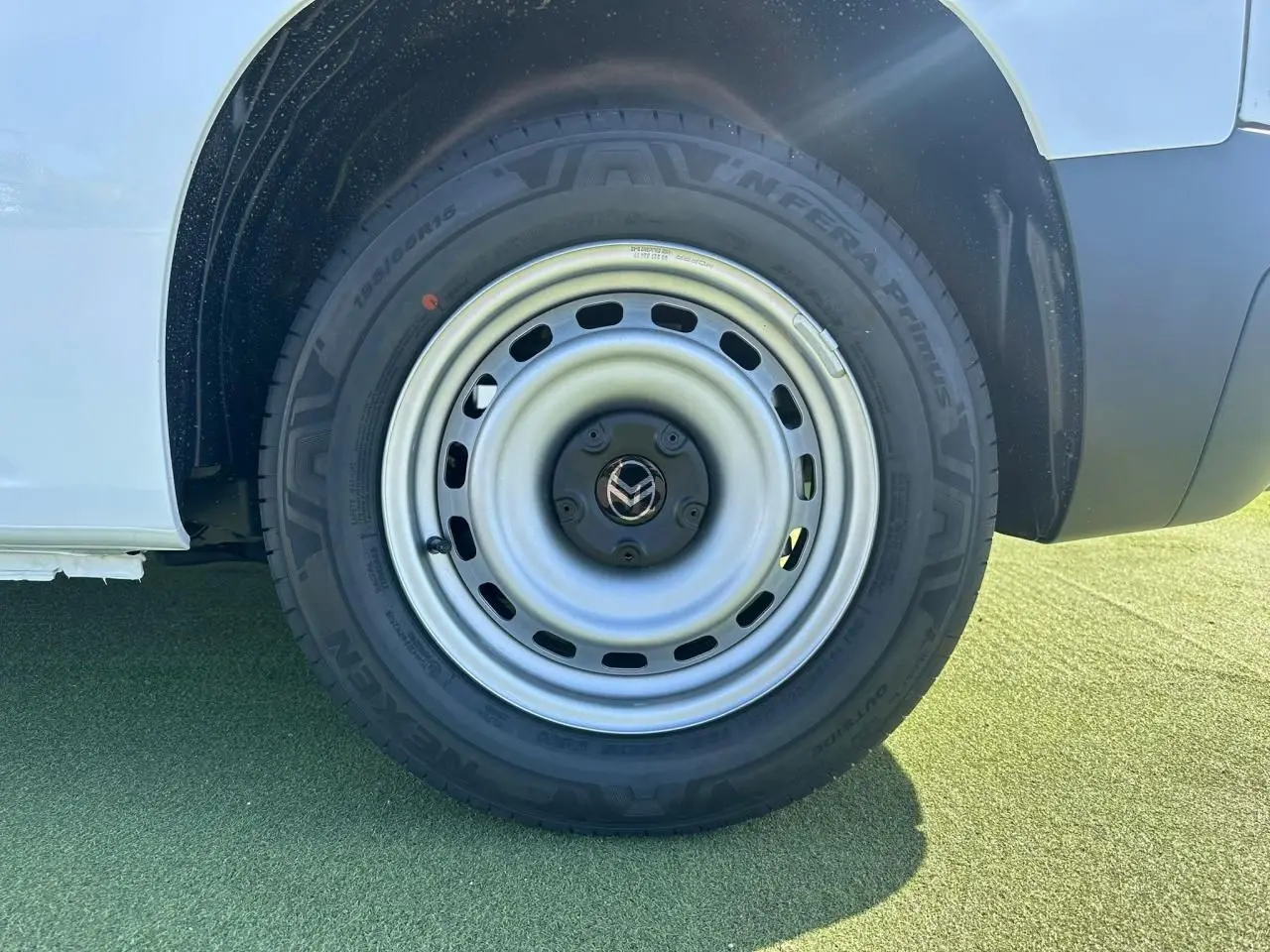 Gros plan sur la roue arrière droite en jante tôle grise du Citroën Berlingo blanc Icy, avec partie basse de la carrosserie visible.
