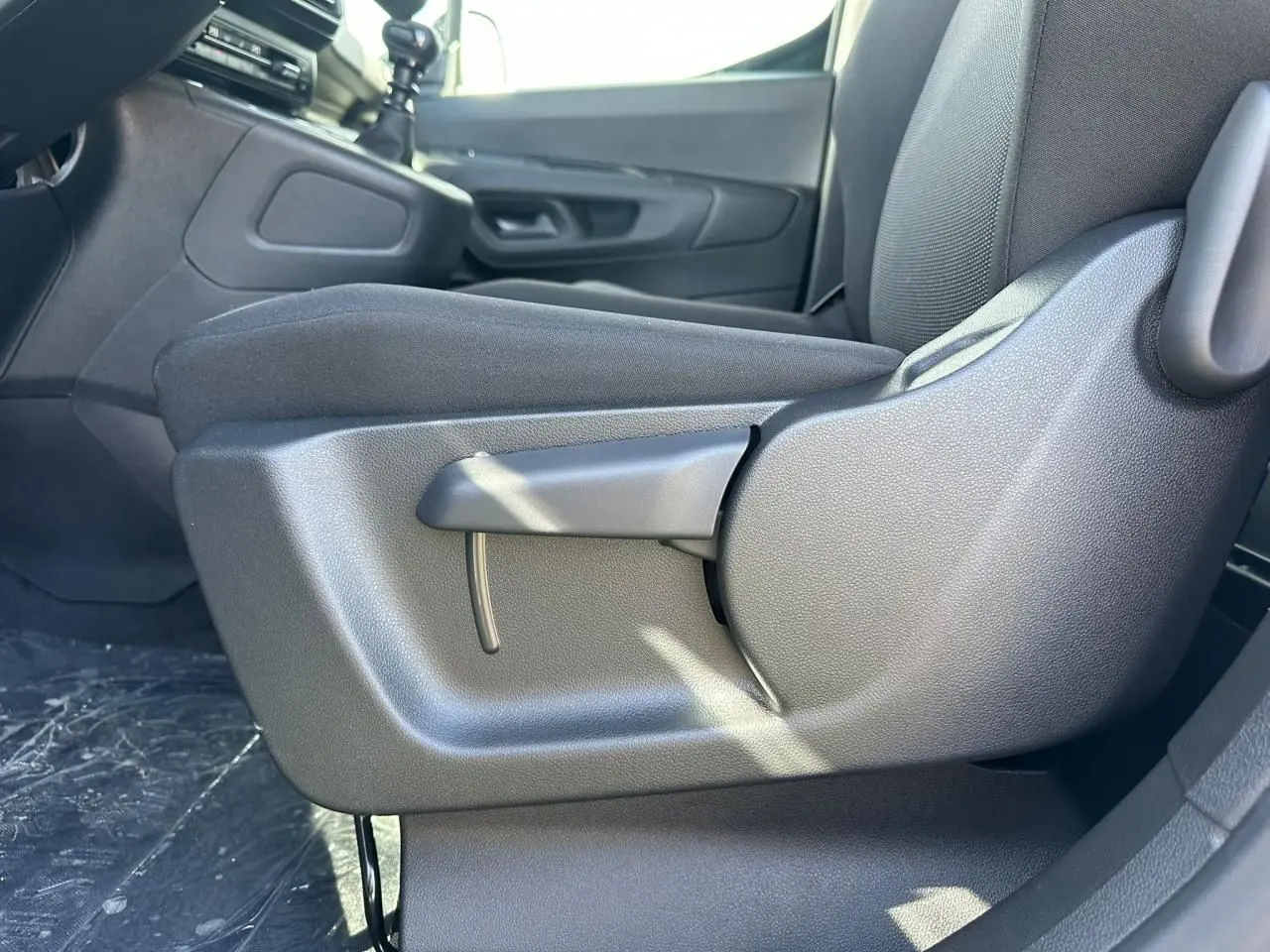 Gros plan sur le réglage manuel du siège conducteur en tissu noir dans l'habitacle du Citroën Berlingo blanc Icy.