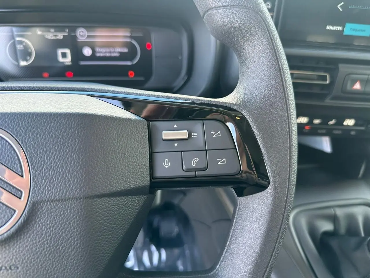 Gros plan sur les commandes du volant noir du Citroën Berlingo blanc Icy, avec tableau de bord numérique en arrière-plan.