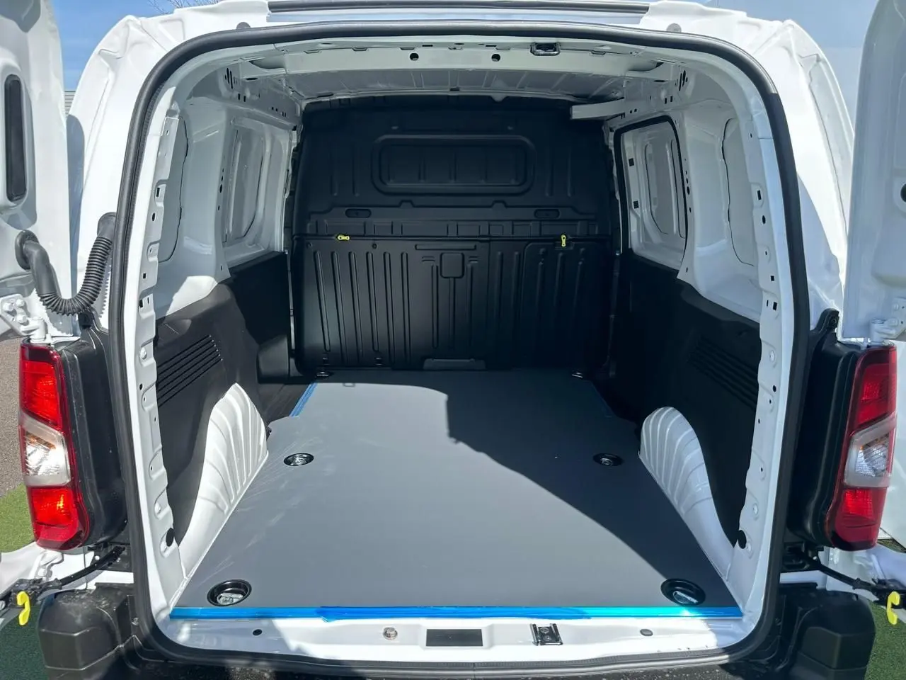 Vue arrière ouverte du Citroën Berlingo blanc Icy montrant l'espace de chargement avec plancher plat et anneaux d'arrimage.