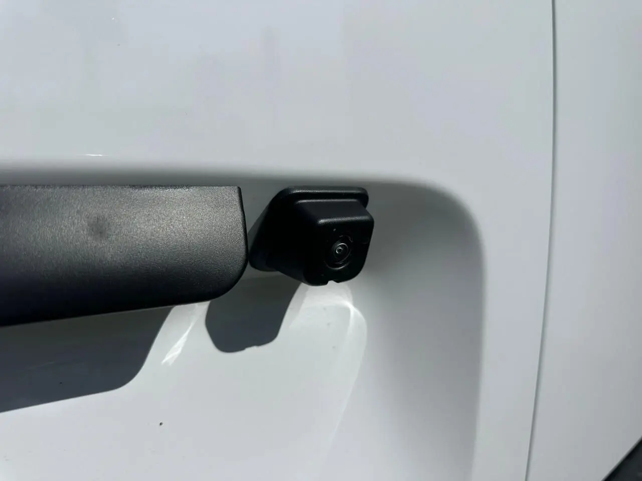 Gros plan sur la caméra de recul noire intégrée à la porte latérale droite du Citroën Berlingo blanc Icy.