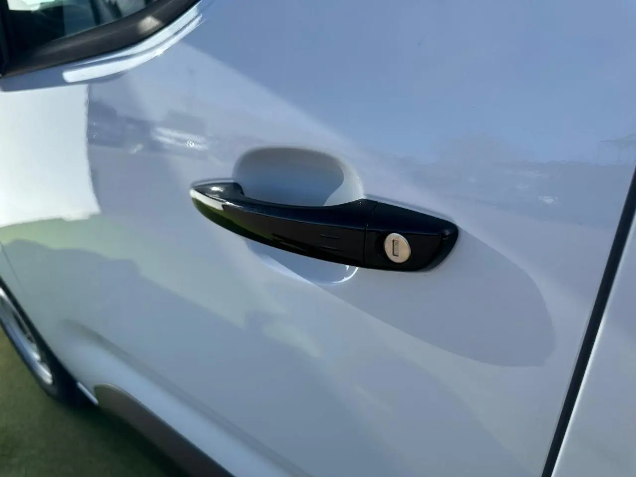 Poignée de porte noire brillante sur la porte avant gauche du Citroën Berlingo III blanc Icy, vue rapprochée en extérieur.