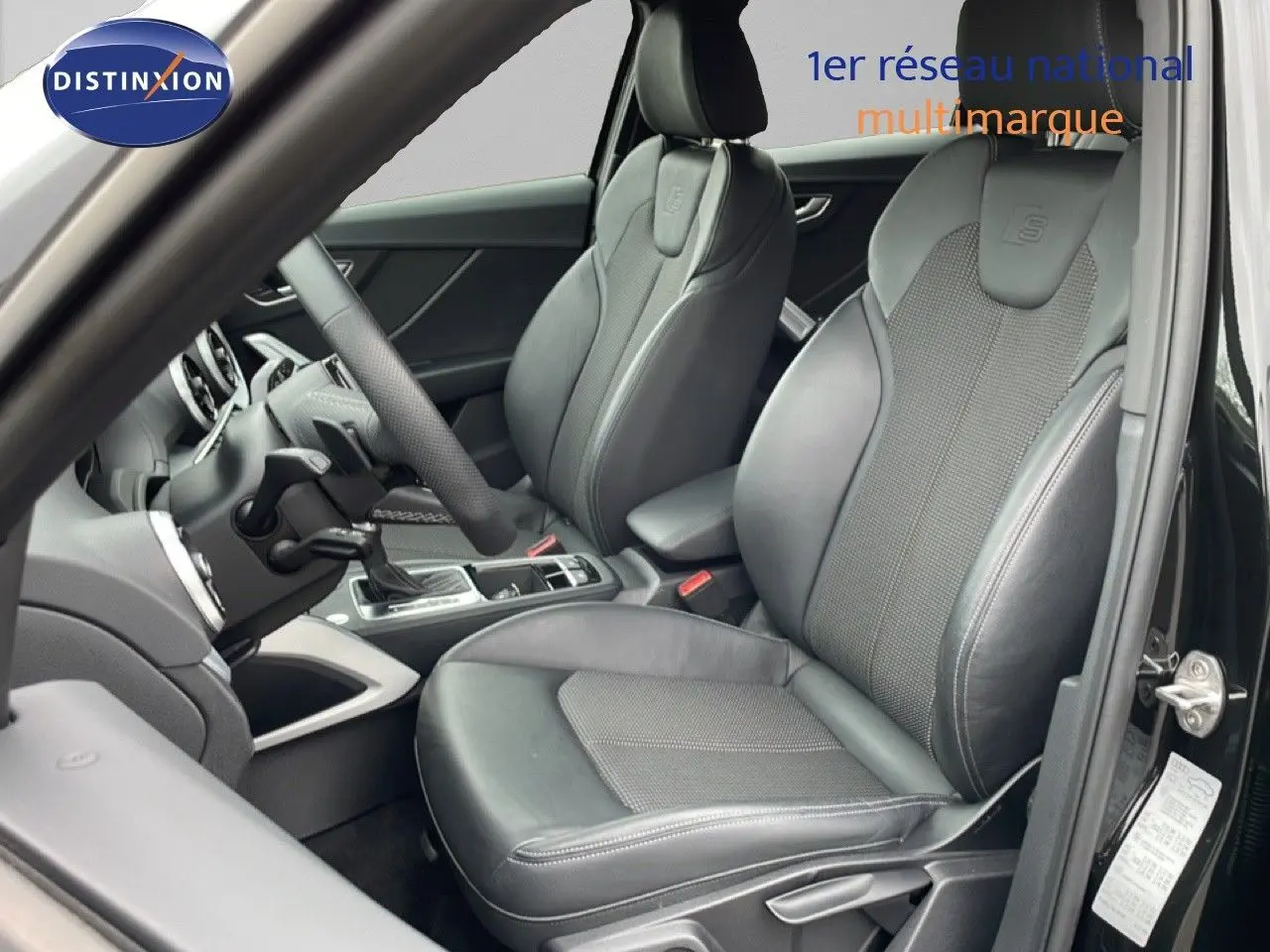 Vue intérieure côté conducteur de l'Audi Q2 S-Line 2025 avec sièges en cuir noir et volant multifonction.