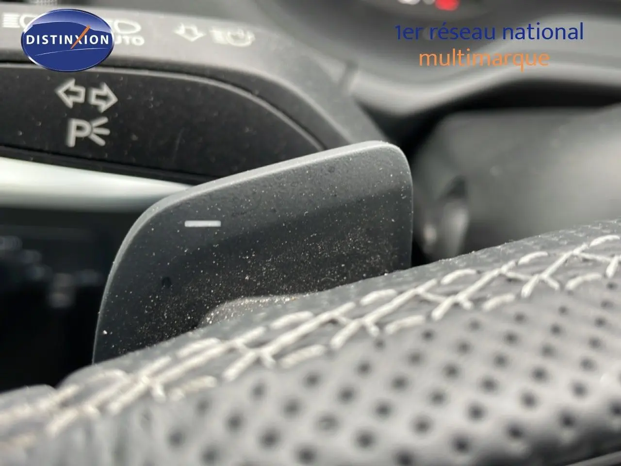 Gros plan sur la palette de changement de vitesse derrière le volant en cuir perforé d’un Audi Q2 noir mito metal.