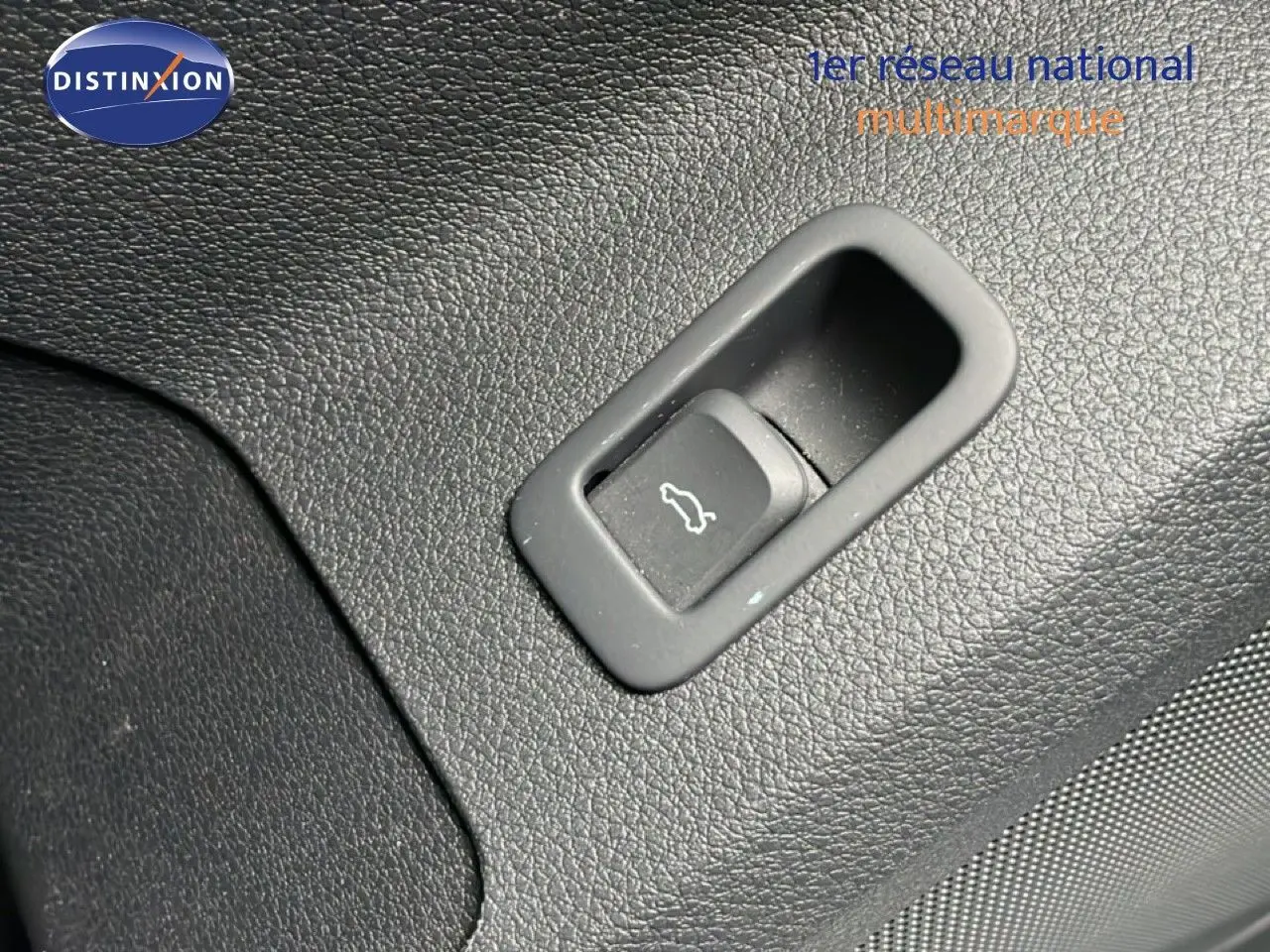 Bouton d'ouverture du coffre sur panneau intérieur noir texturé d'un Audi Q2 noir mito metal, vue rapprochée.
