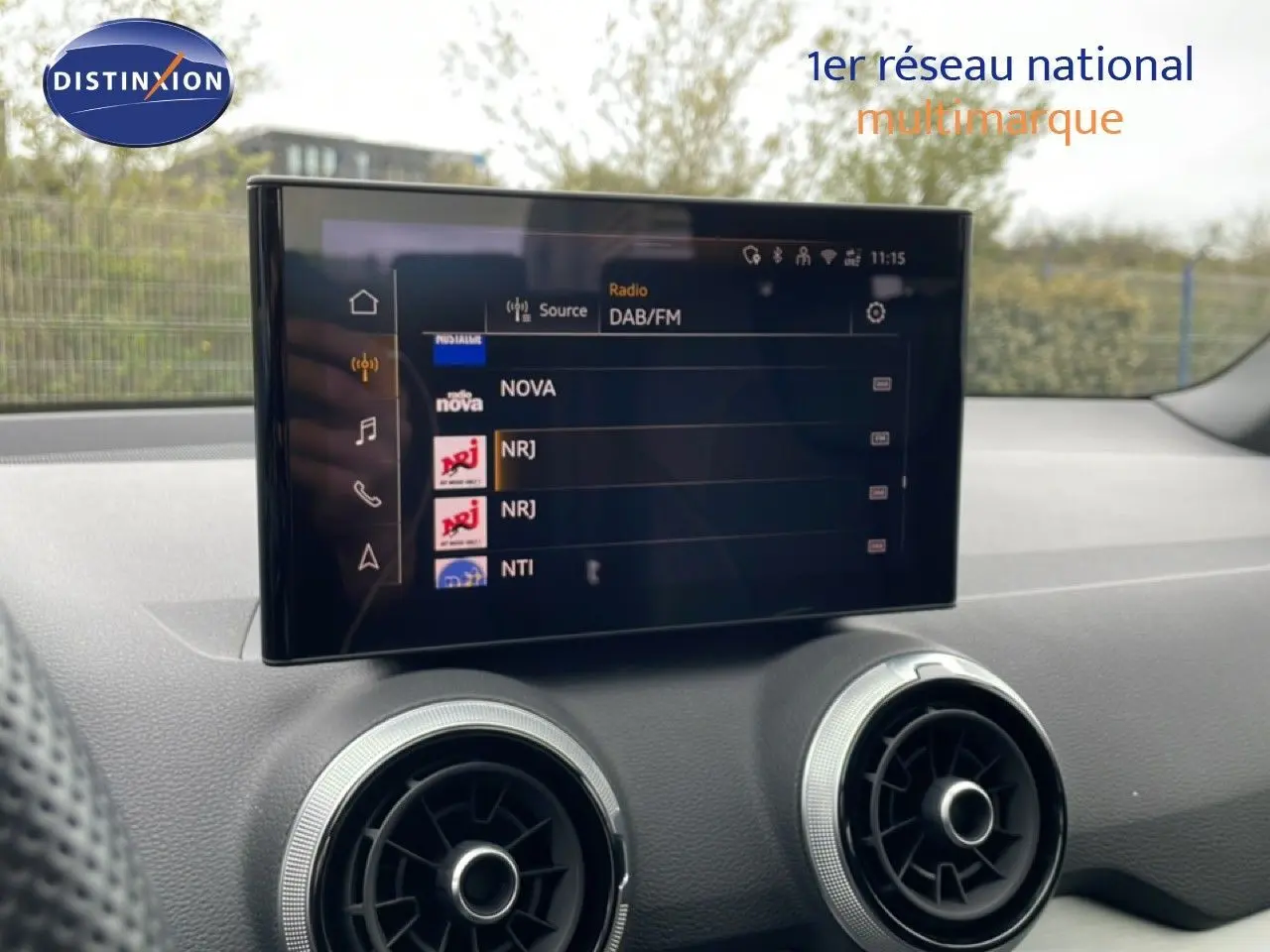 Écran tactile central affichant les stations radio, avec aérateurs ronds argentés sur tableau de bord noir.