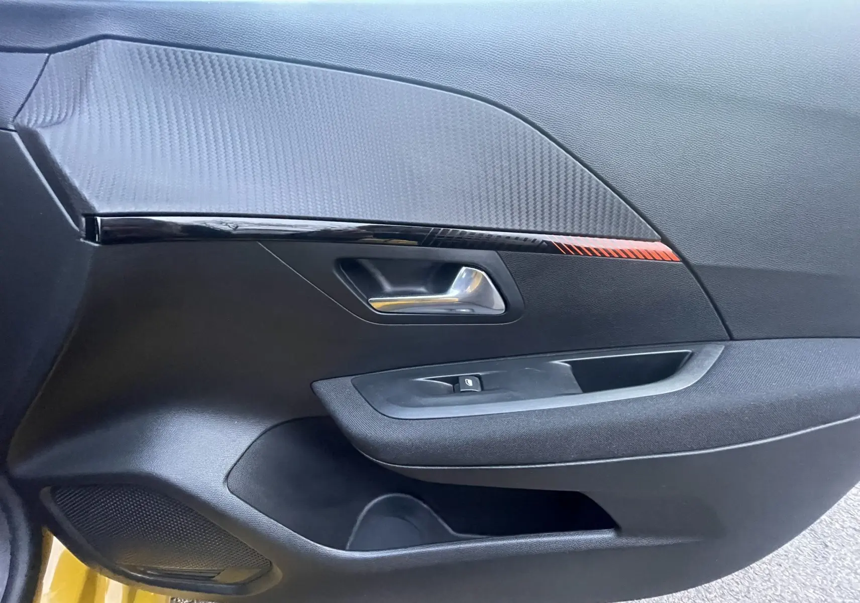 Détail de la porte côté conducteur de la Peugeot 208 II électrique jaune 2023 avec insert décoratif noir et rouge.