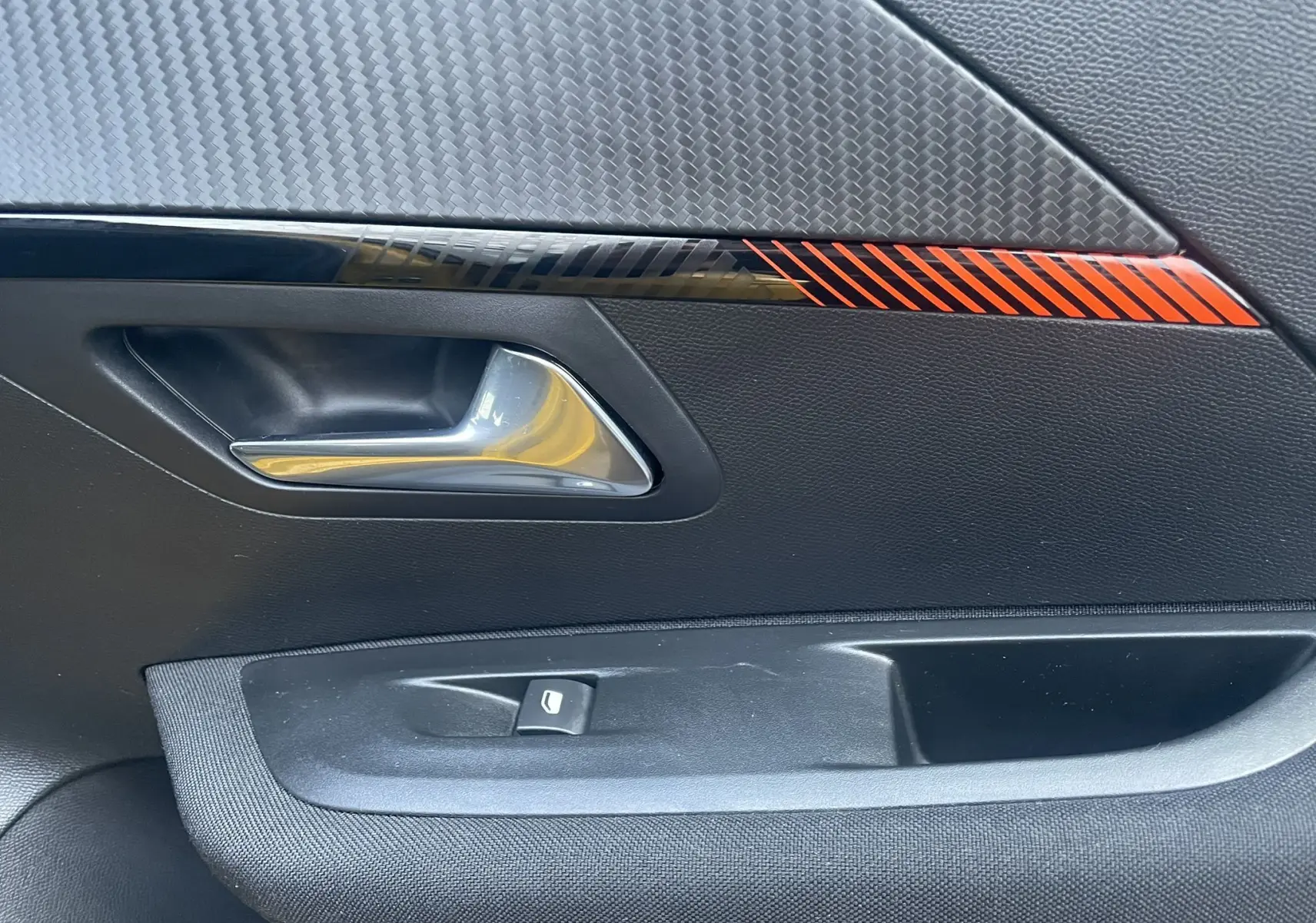 Détail de la poignée intérieure côté gauche de la porte d'une Peugeot 208 électrique jaune 2023 avec insert décoratif rouge.